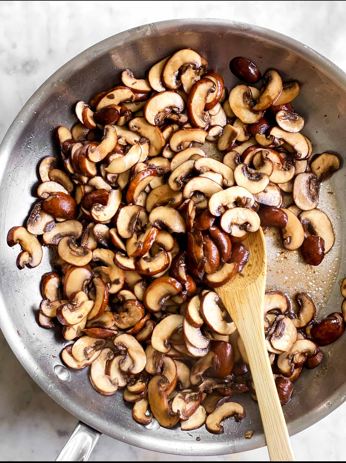 overhead view of slightly cooked and seasoned mushrooms in skillet with wooden spoon