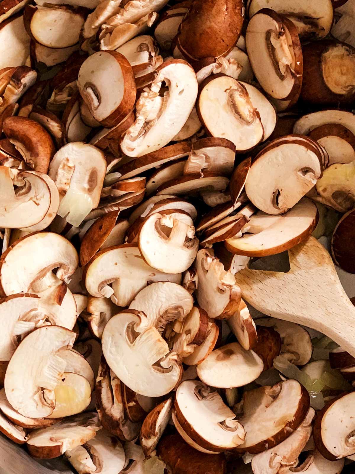 overhead close up of raw sliced mushrooms with wooden spoon