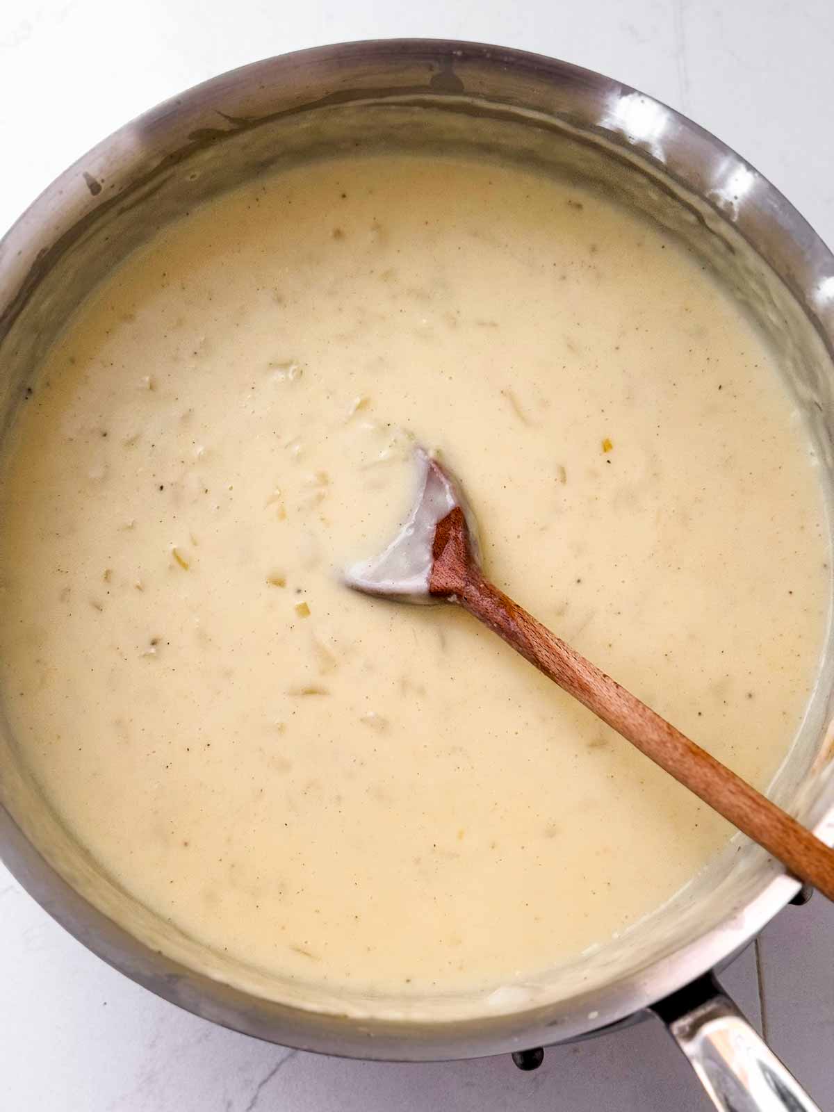 overhead view of finished sauce for scalloped potatoes in saucepan with wooden spoon