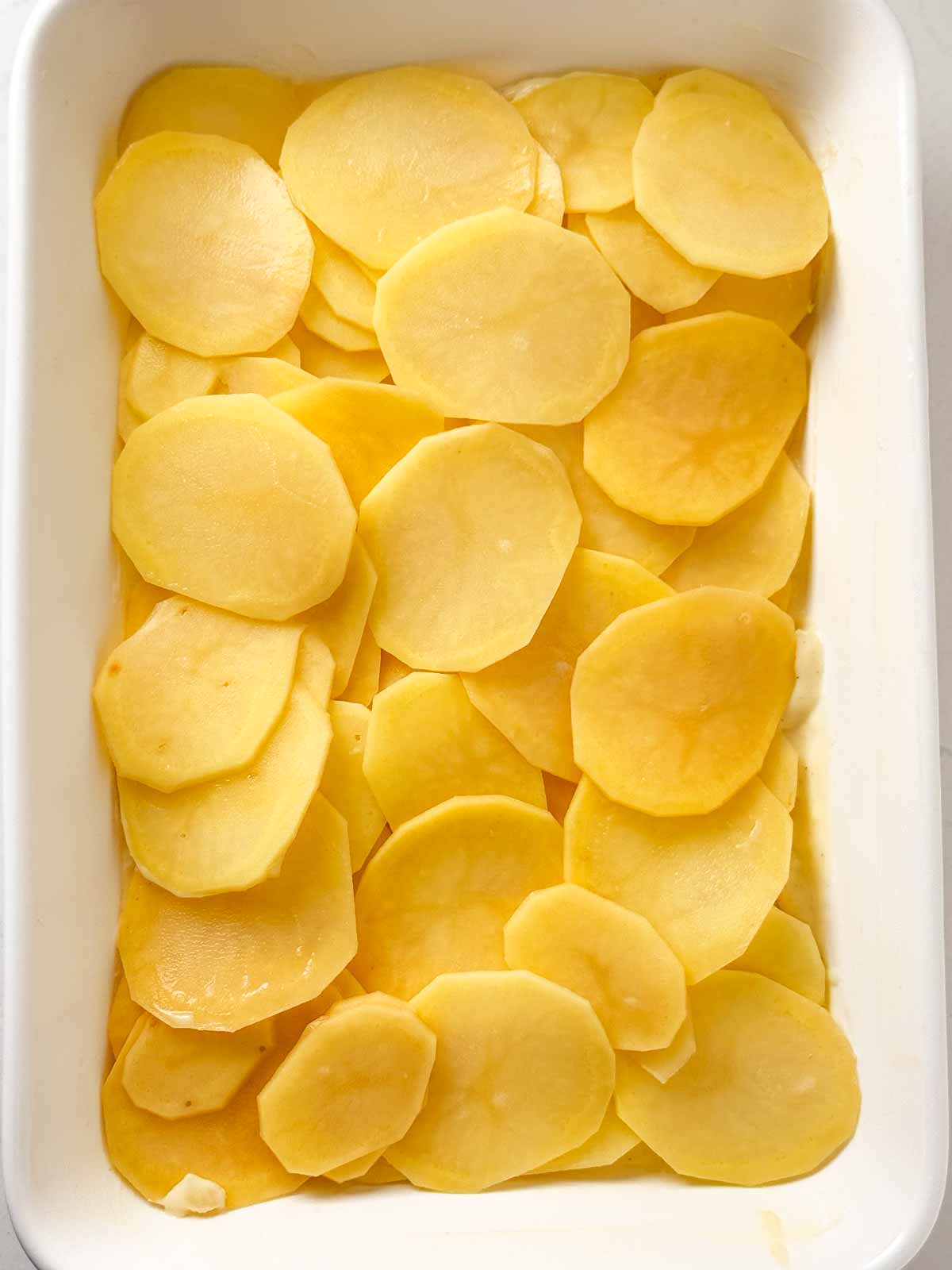 overhead view of sliced potatoes in white casserole dish