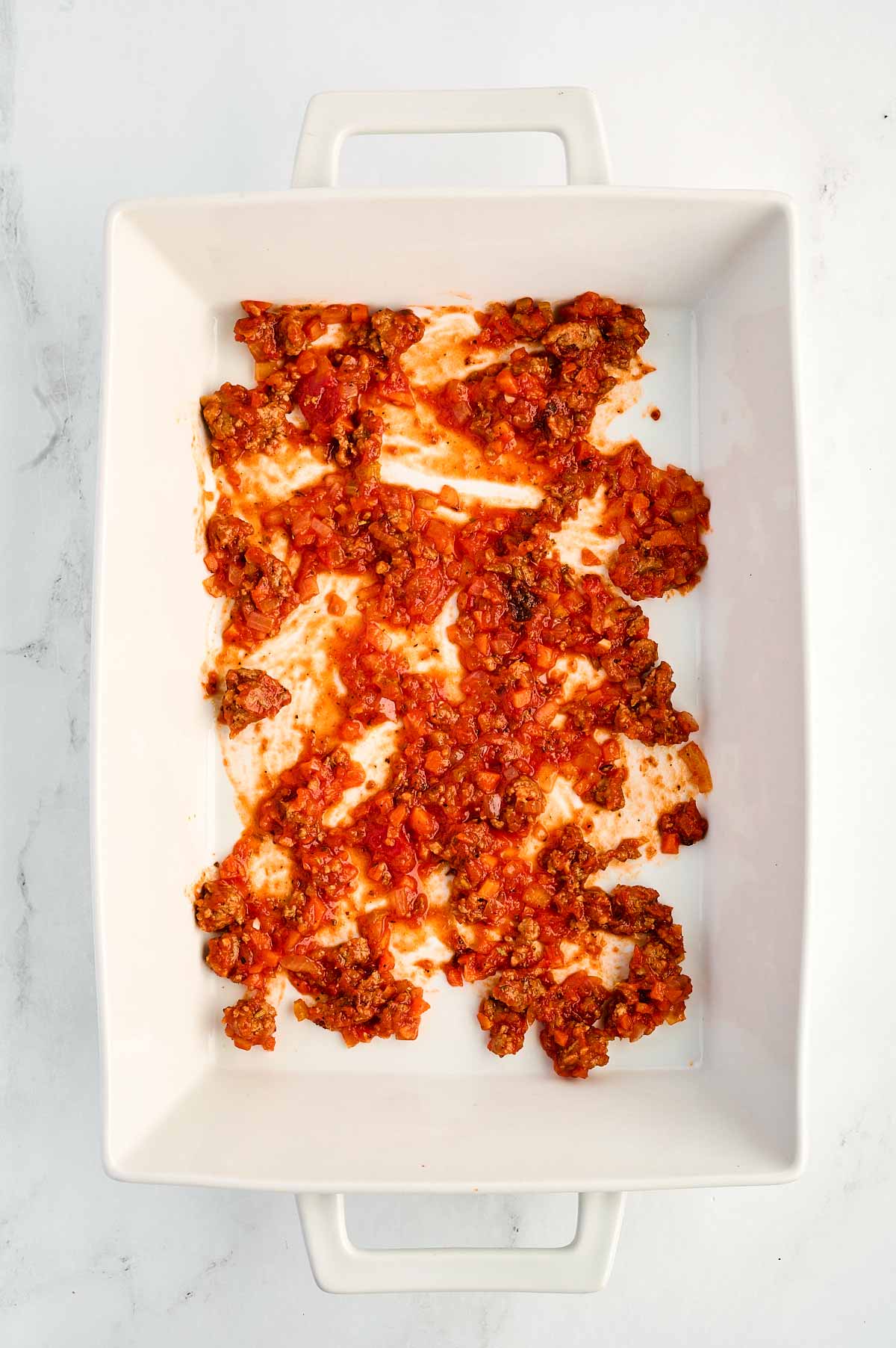 overhead view of tomato sauce spread in white casserole dish