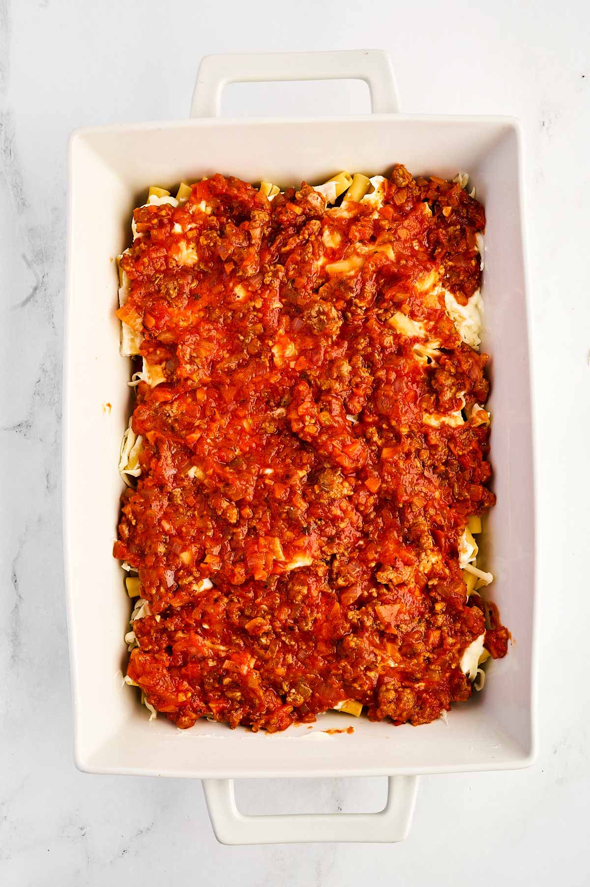 overhead view of cooked pasta with tomato sauce in white casserole dish