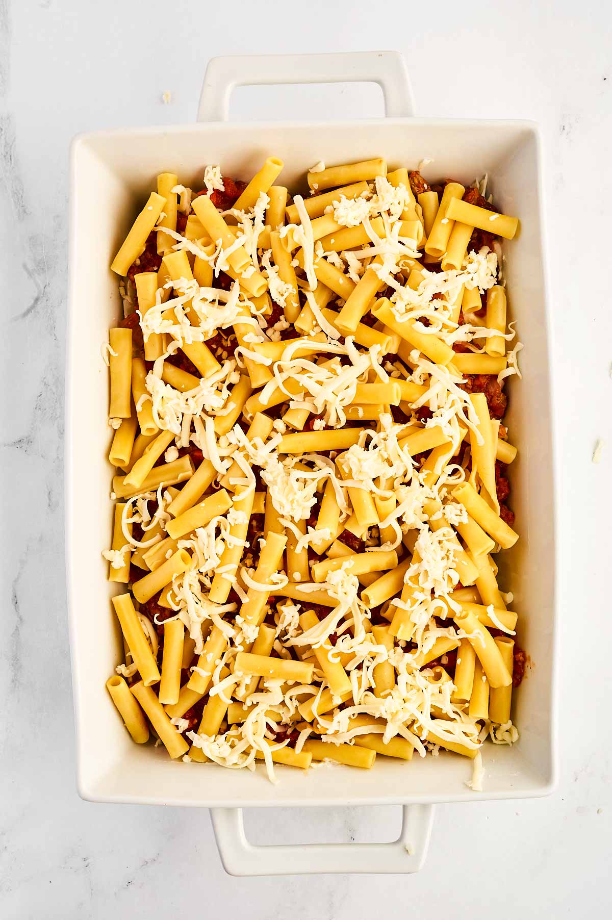 overhead view of cooked pasta with cheese over meat sauce in white casserole dish