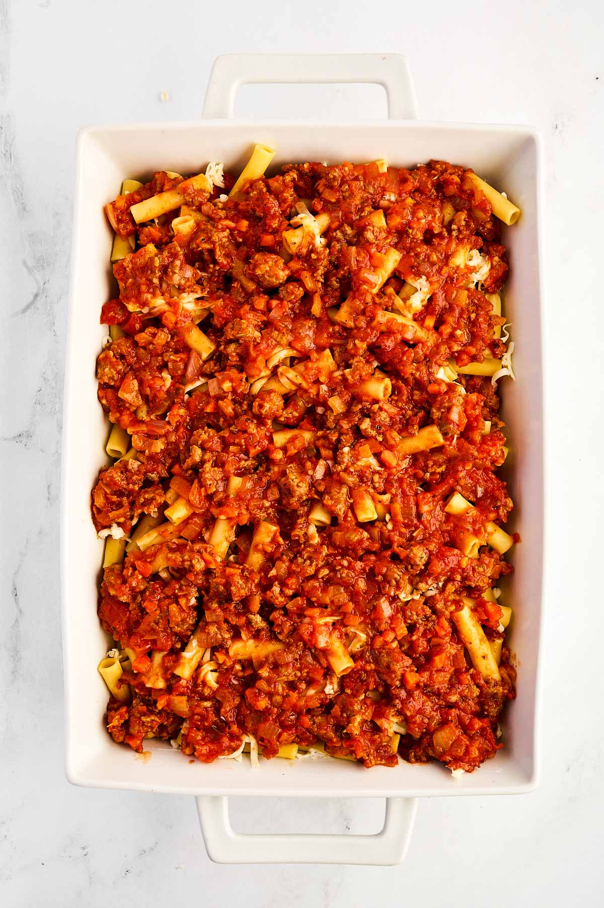 overhead view of cooked pasta topped with meat sauce in white casserole dish