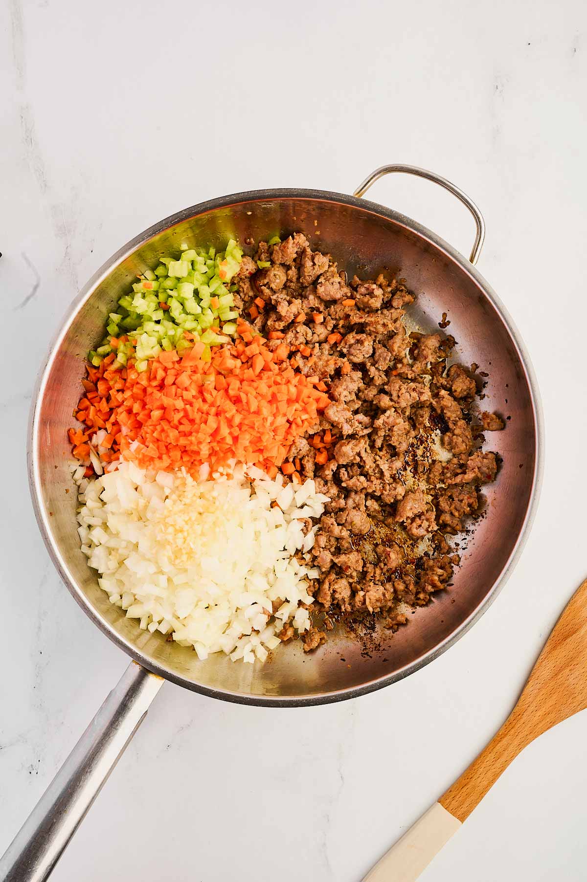 overhead view of cooked sausage in skillet with uncooked sofritto