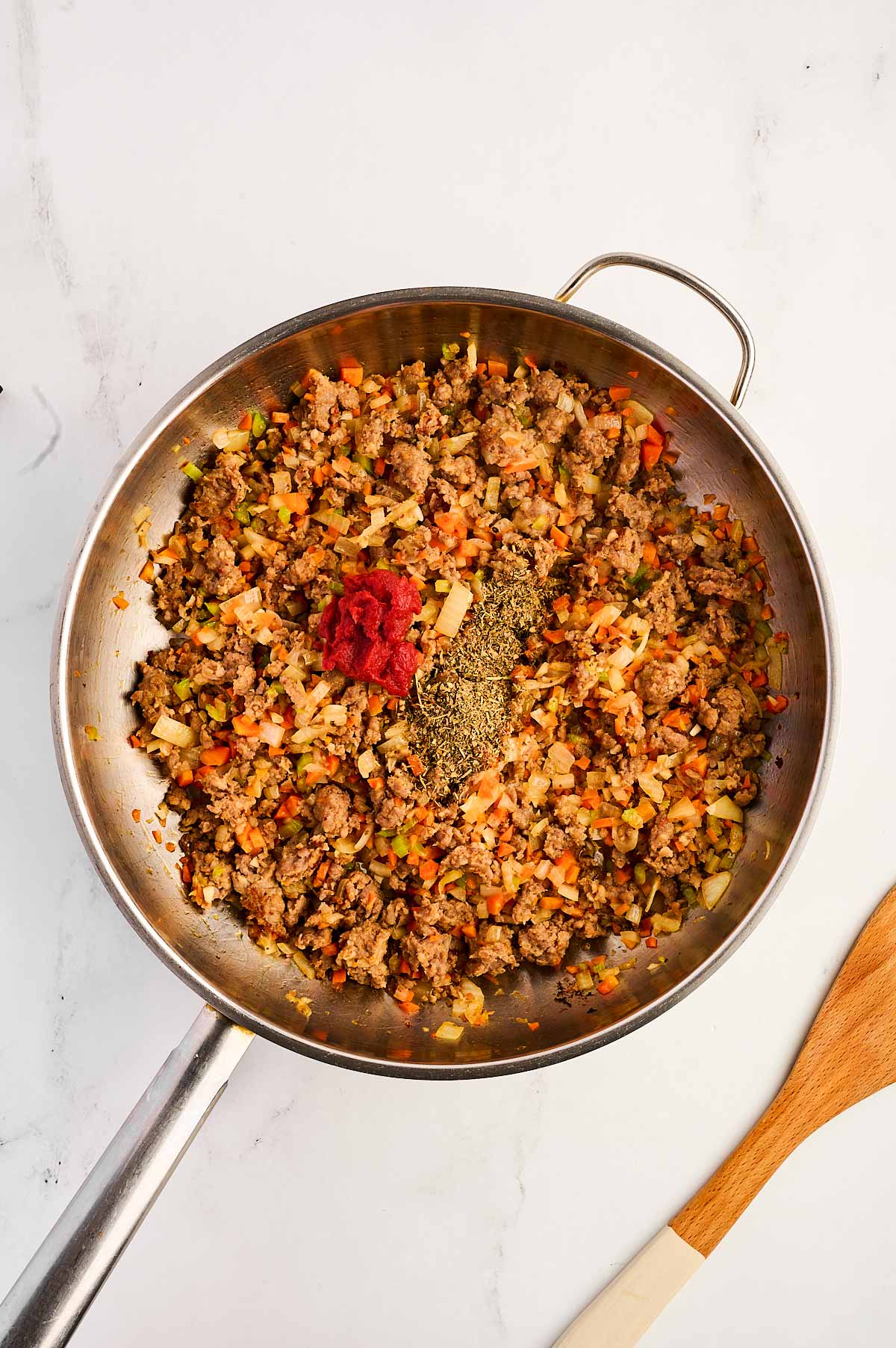 overhead view of cooked sausage and vegetables in skillet with tomato paste and seasoning