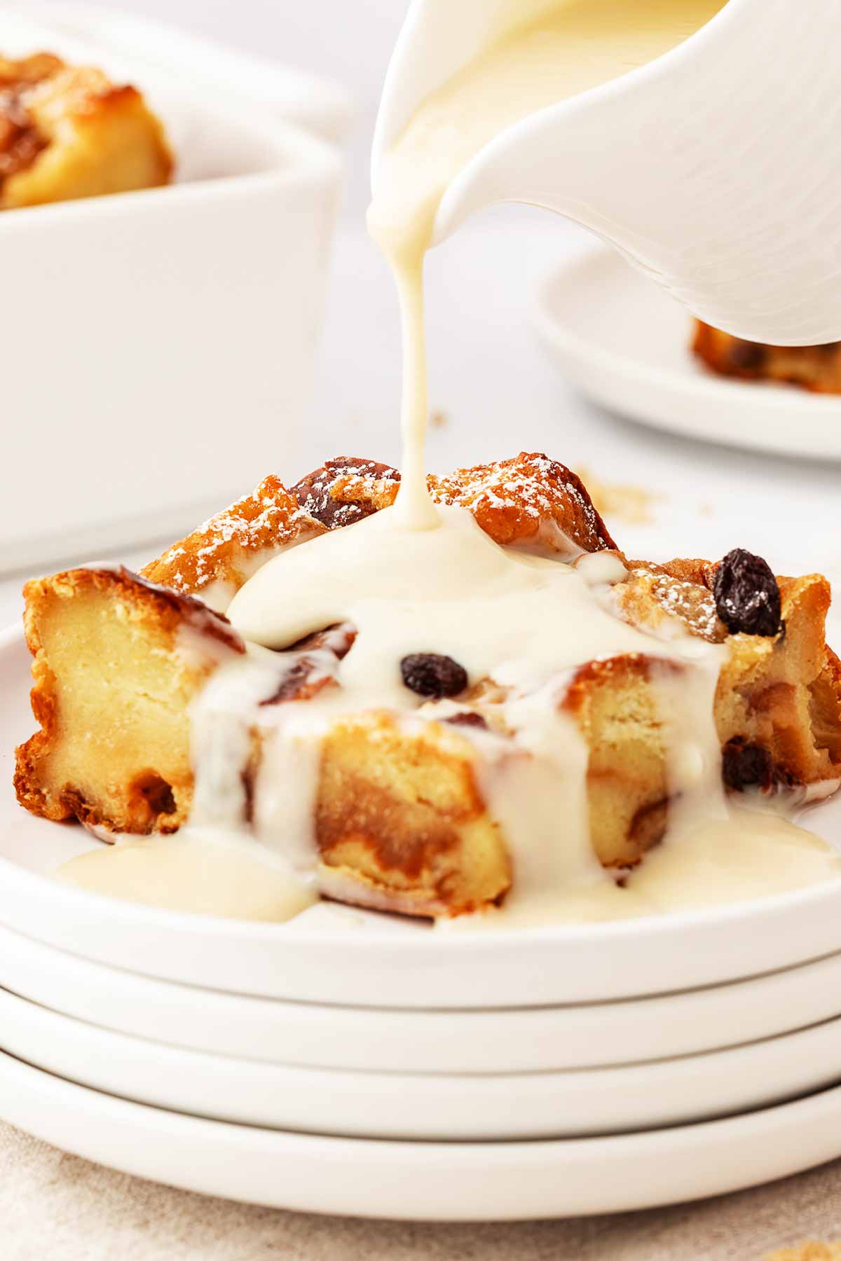 frontal view of custard pouring over slice of bread pudding on white plate