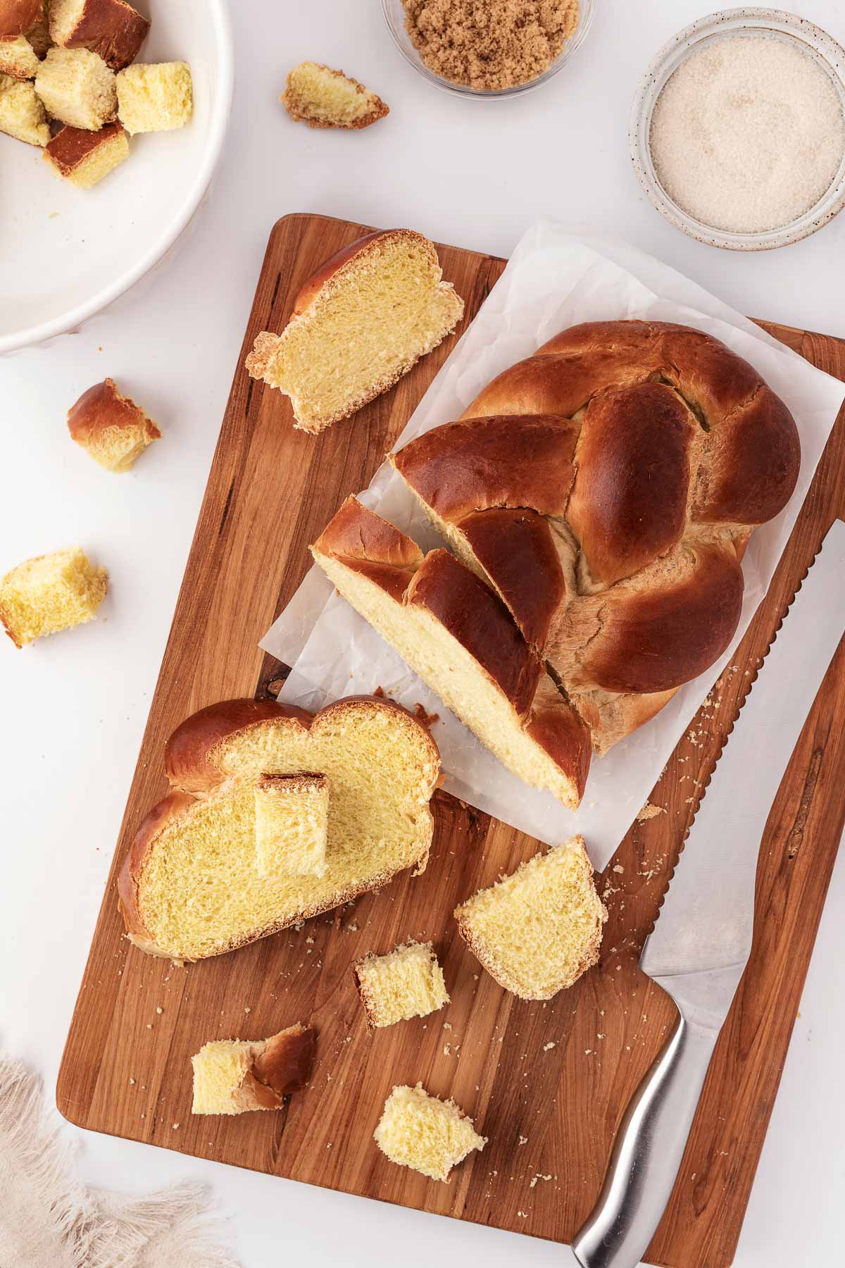 overhead view of challah being sliced on wooden chopping board