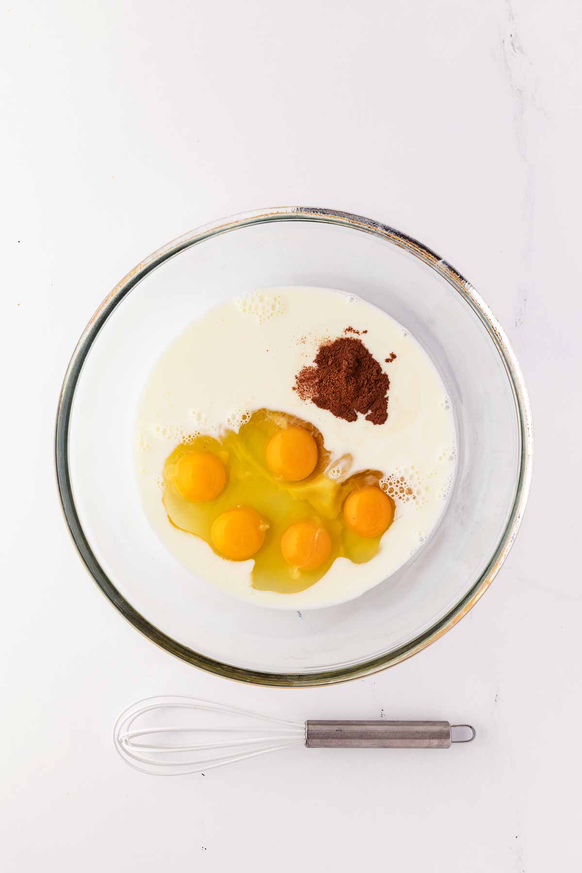 overhead view of eggs, milk and cinnamon in glass bowl