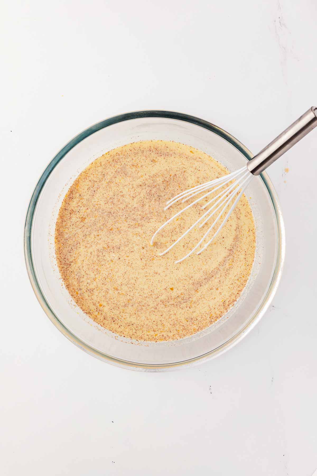 overhead view of custard mix with whisk in glass bowl