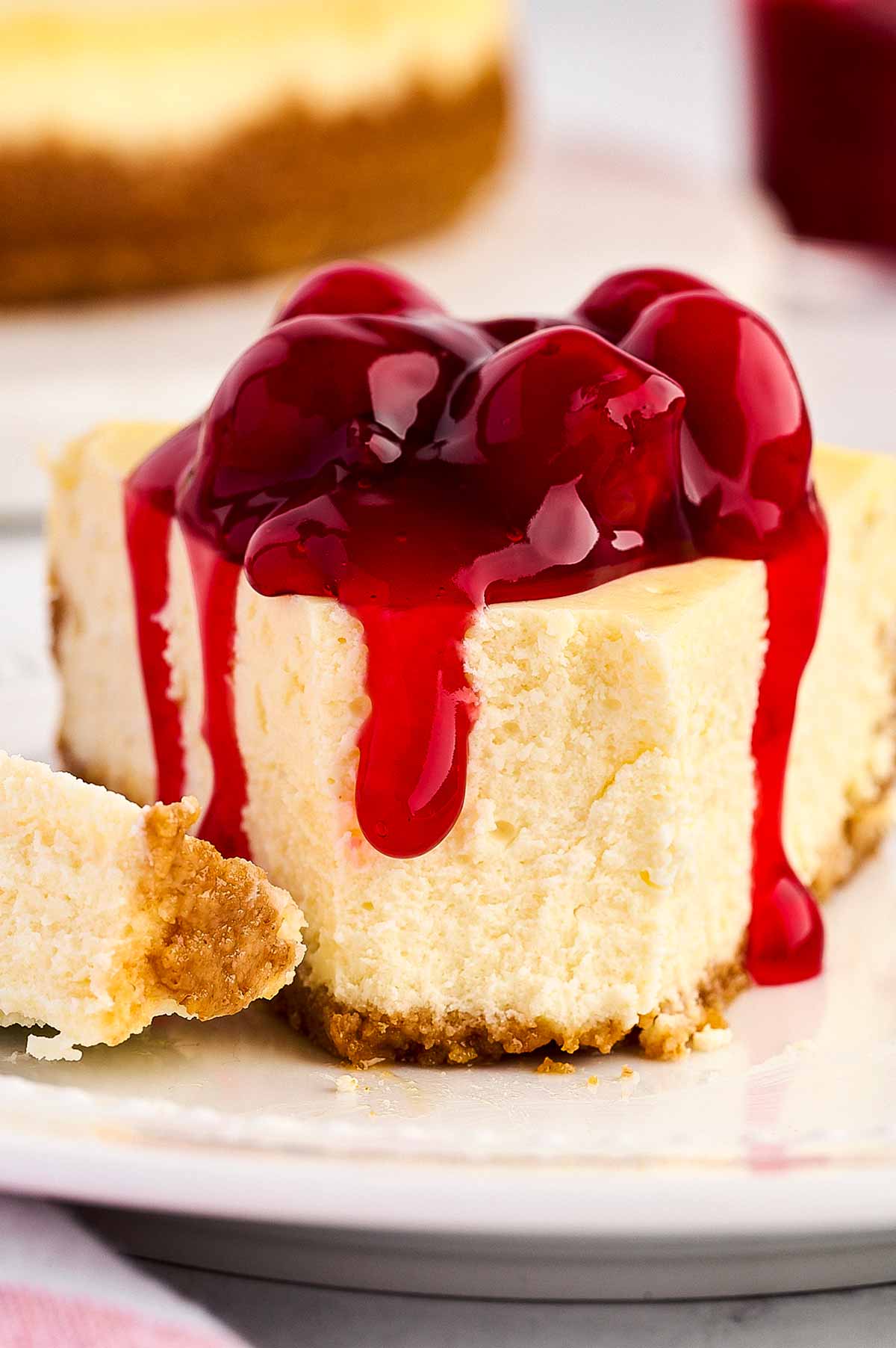 frontal view of cheesecake slice topped with cherry pie filling with bite taken out