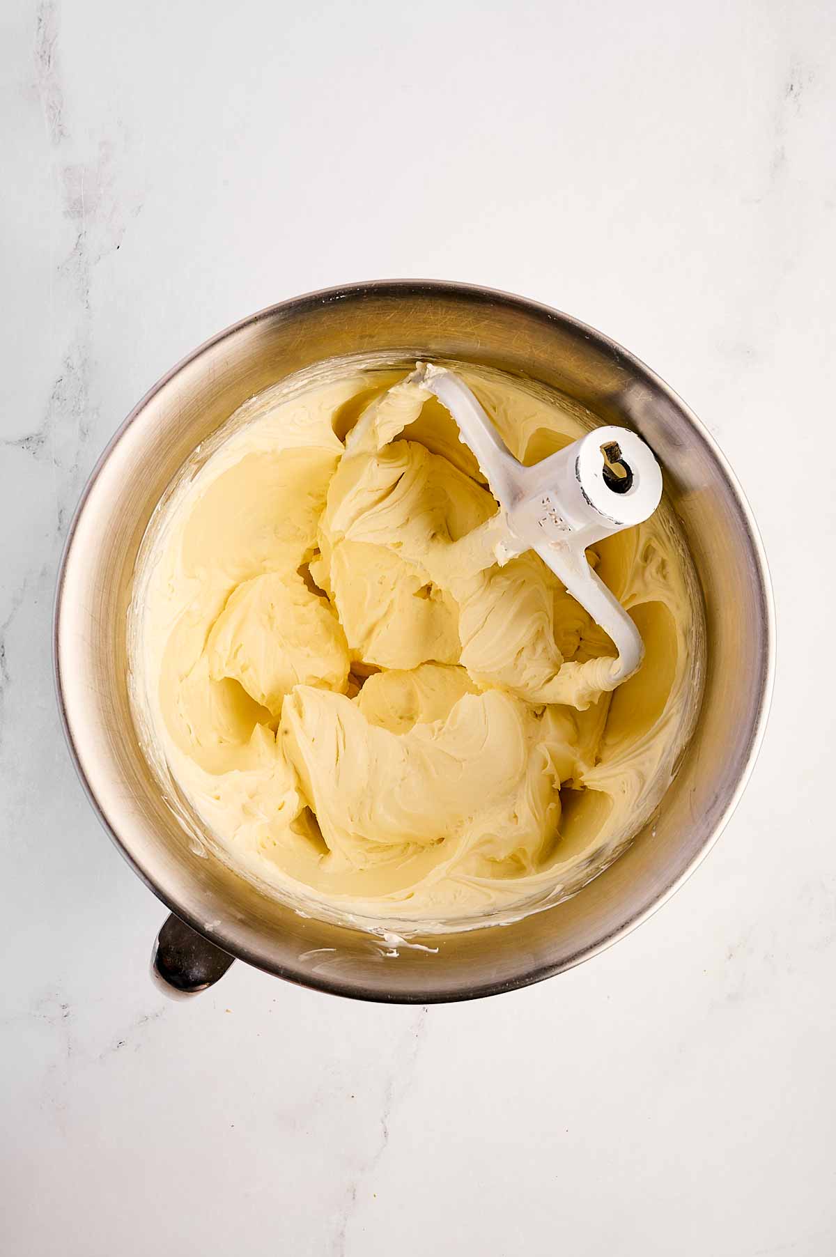 overhead view of cream cheese and sugar mixed together in stand mixer bowl with paddle attachment stuck in