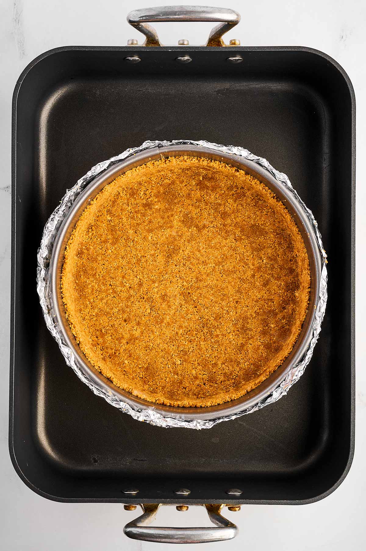 springform pan with graham cracker crust placed inside roasting pan