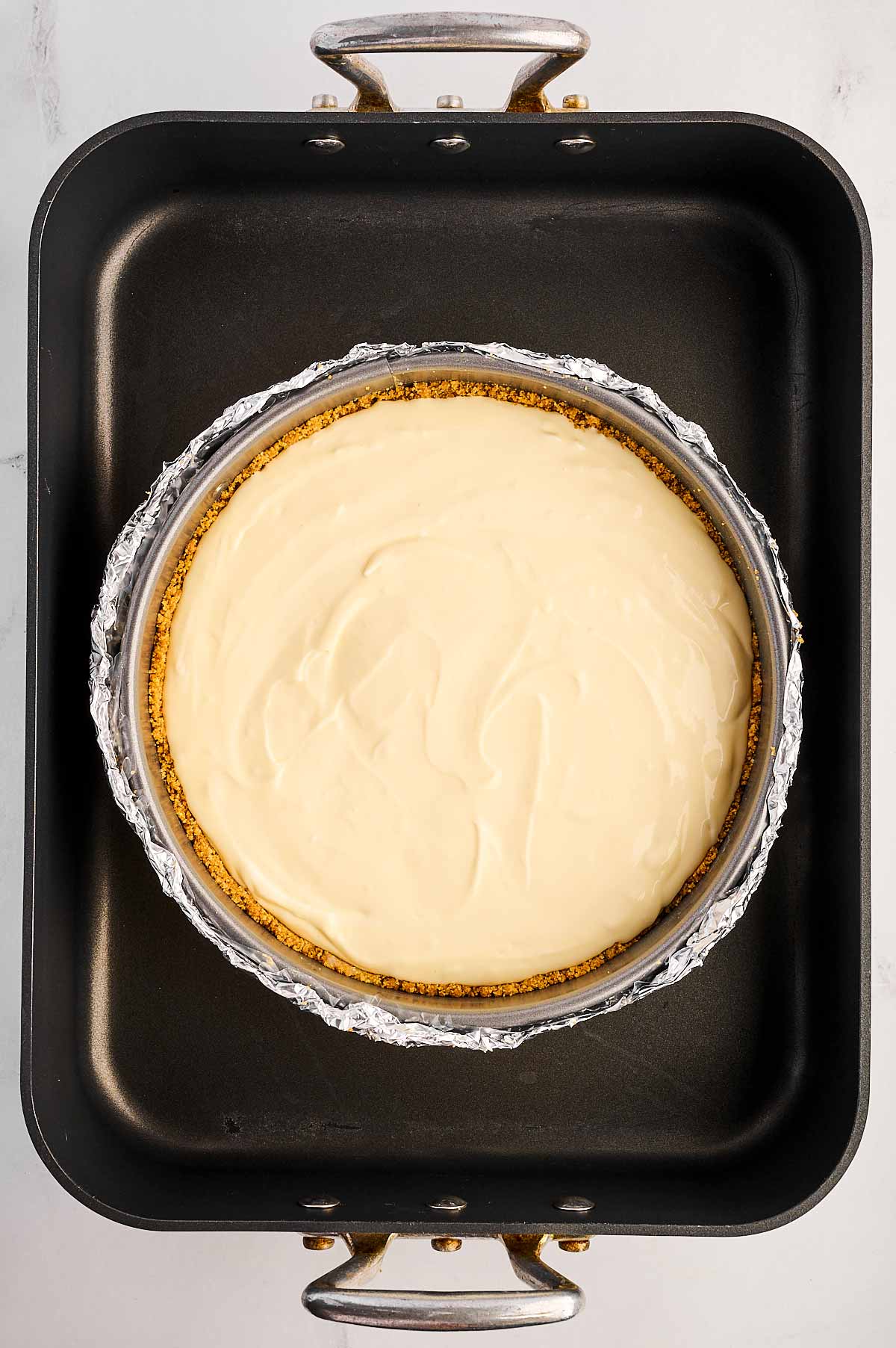 overhead view of springform pan with unbaked cheesecake placed inside roasting pan