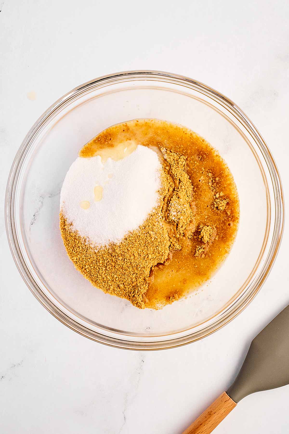 overhead view of graham cracker crumbs, sugar, and melted butter in a glass bowl