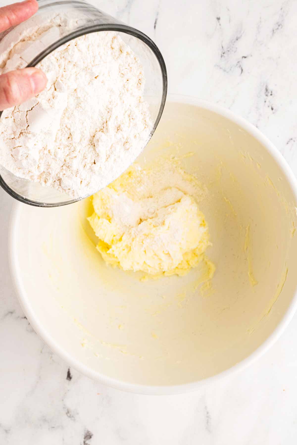 female hands adding flour to butter in mixing bowl