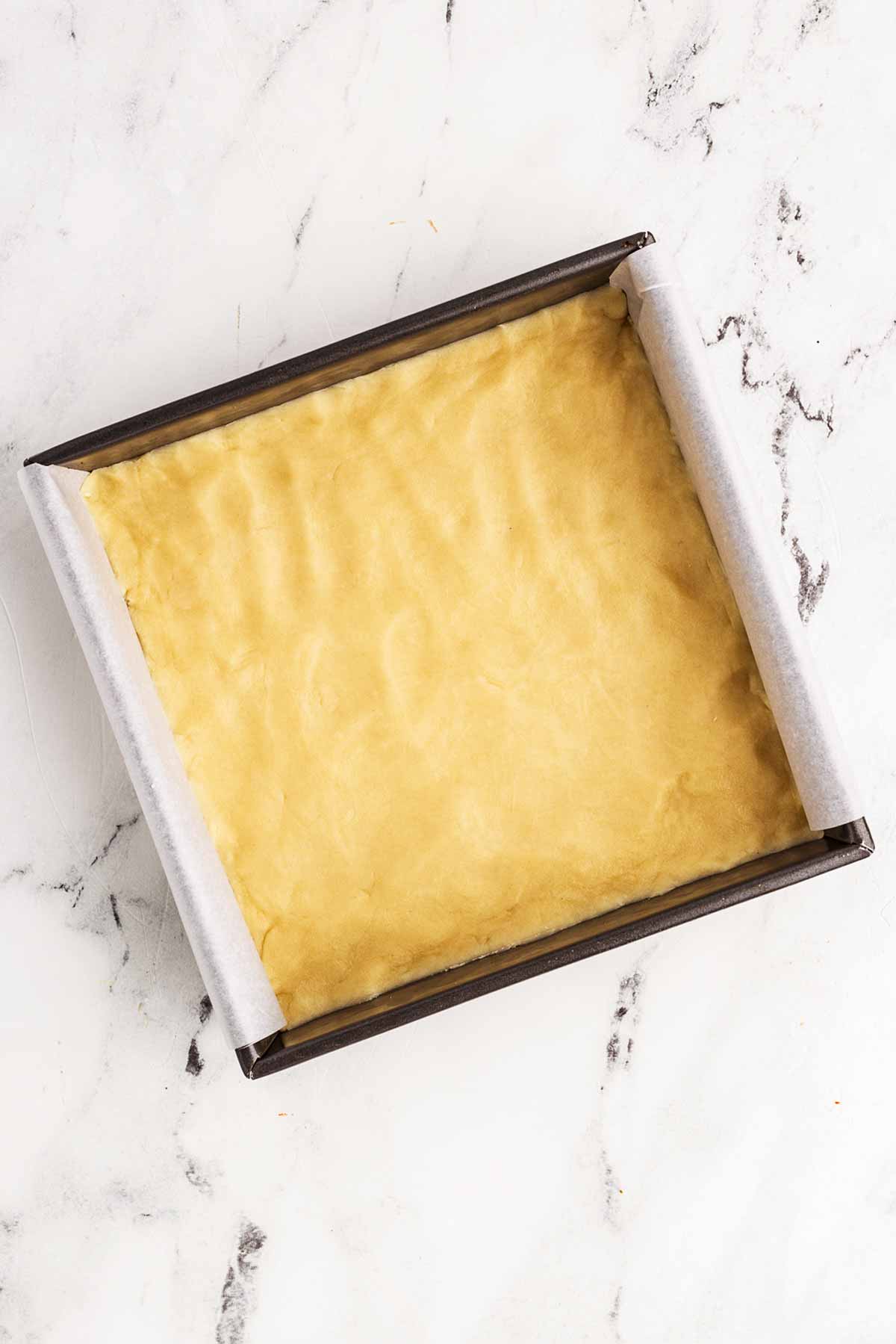 overhead view of lined square baking pan filled with shortbread cookie dough