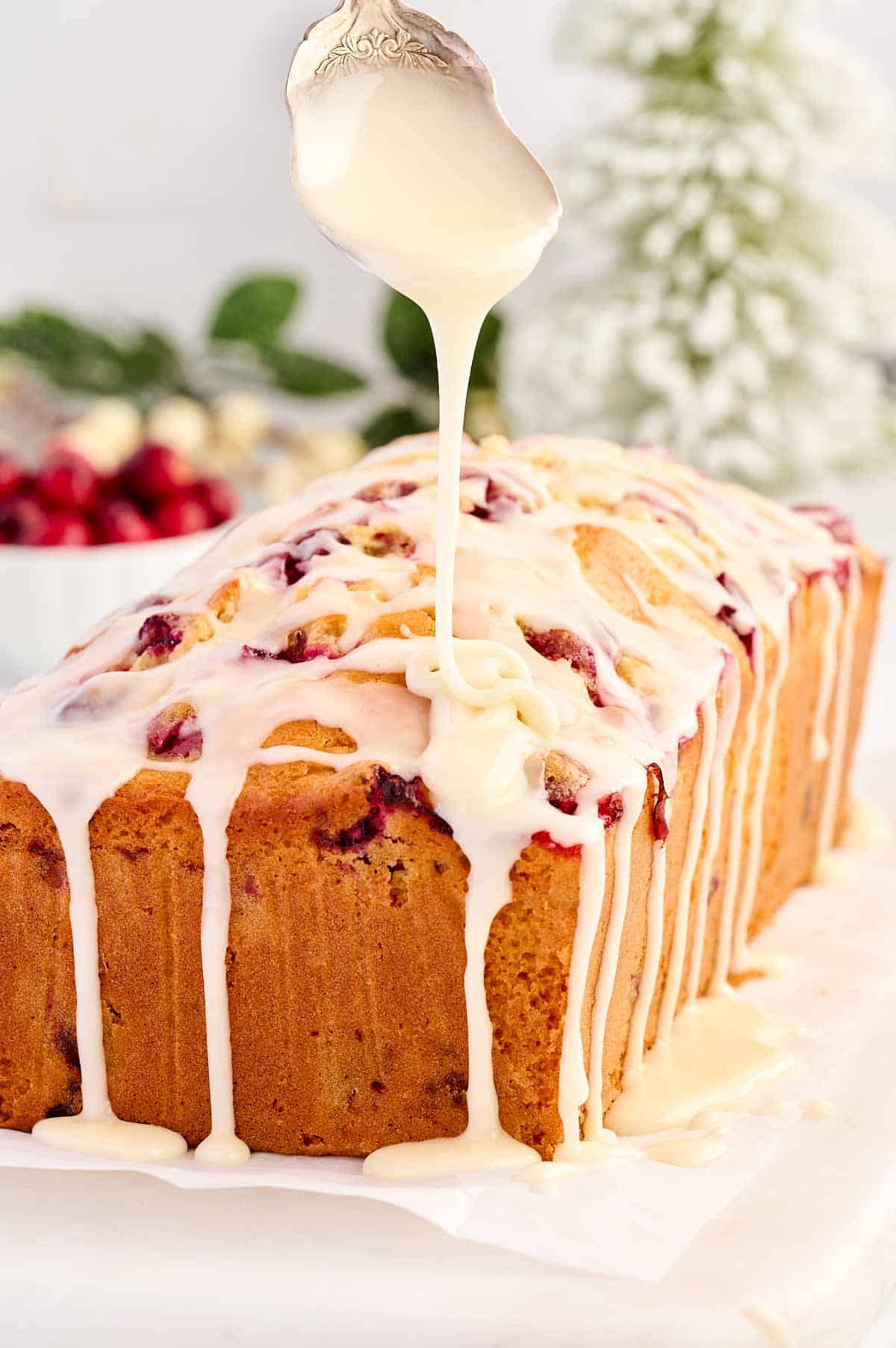 frontal view of glaze drizzling from spoon over cranberry orange bread