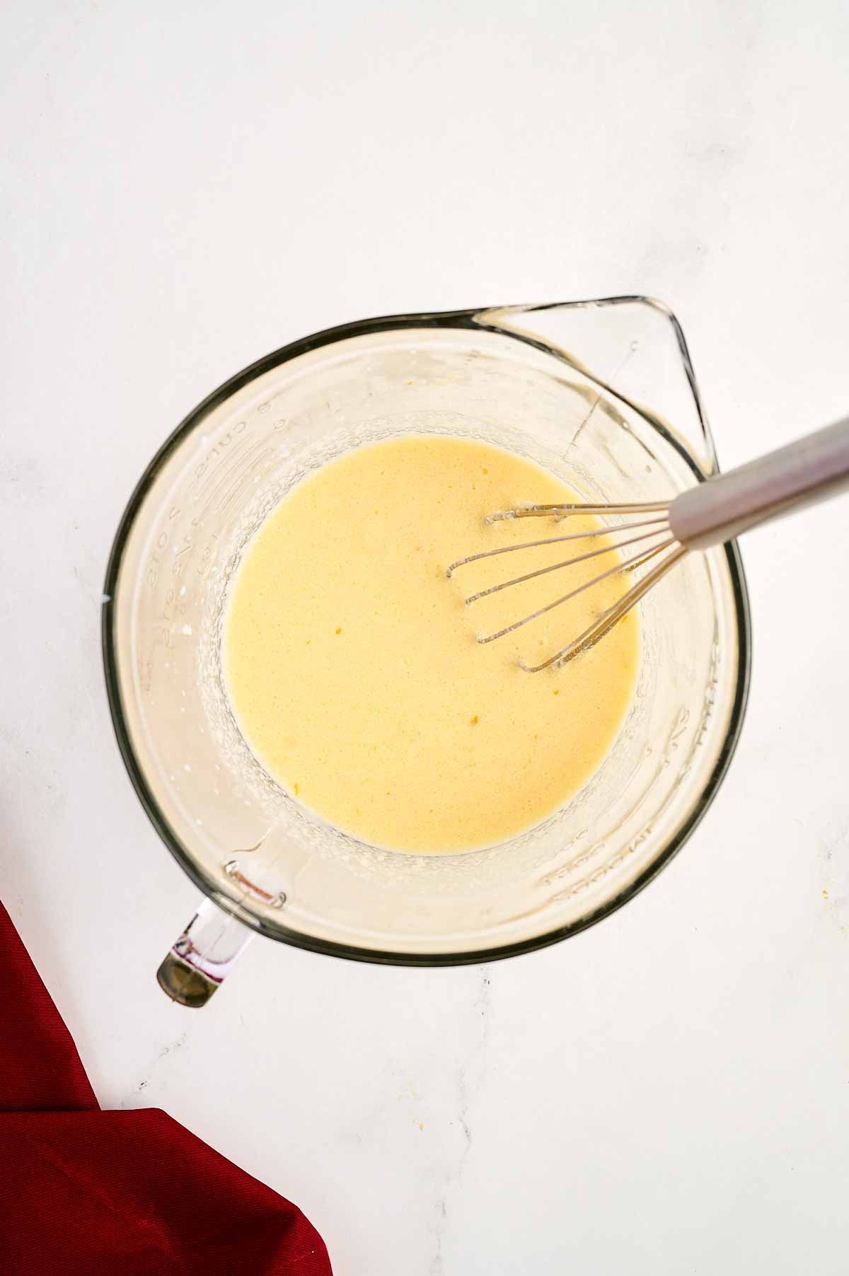 overhead view of wet cake ingredients in glass bowl with whisk