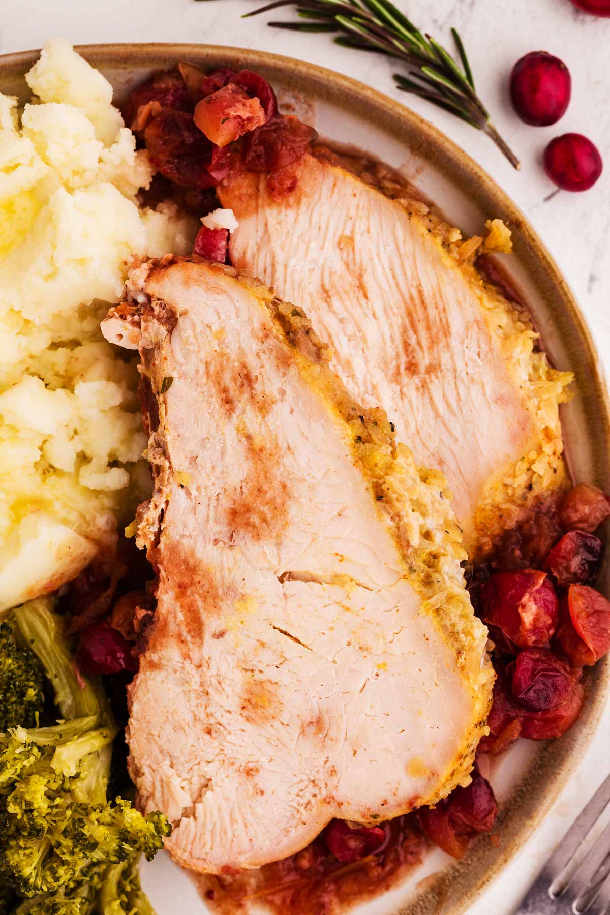 overhead view of sliced cranberry turkey breast on plate with mashed potatoes and broccoli