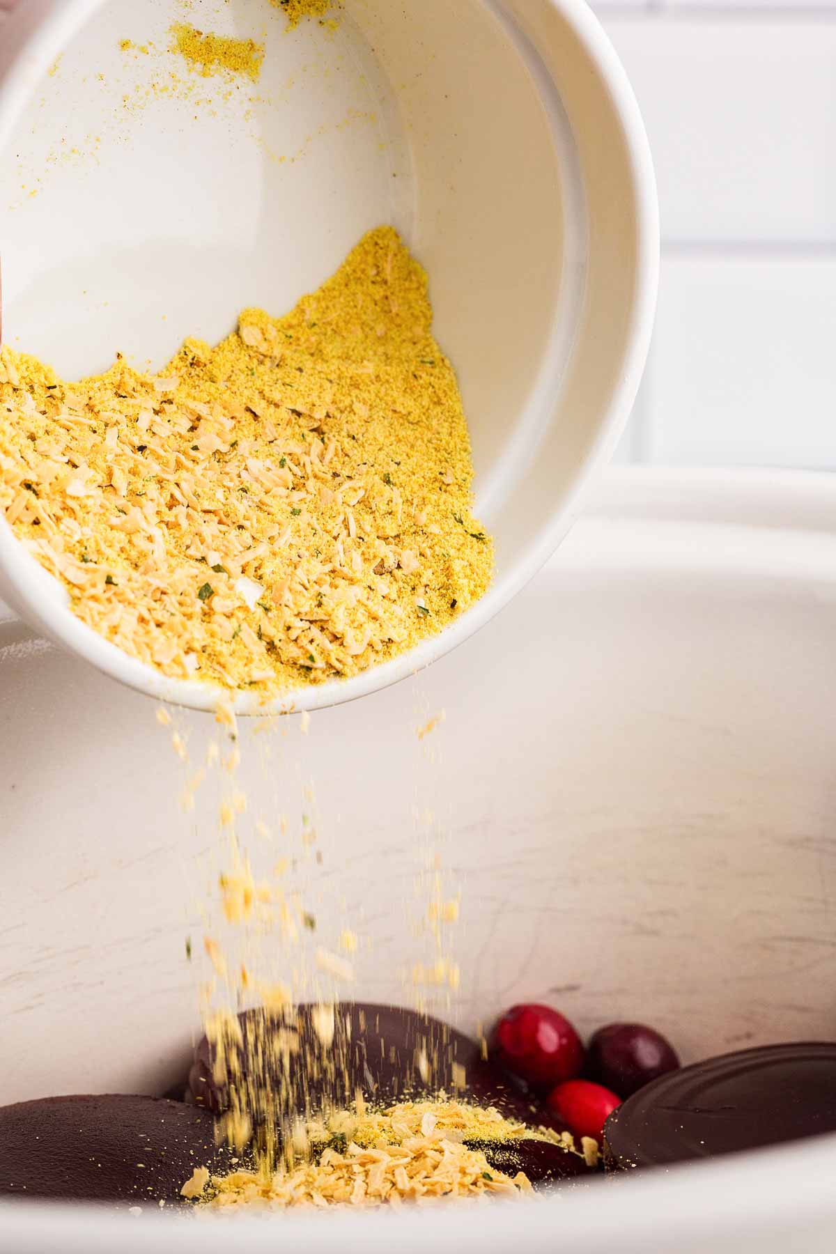 onion soup mix sprinkling from white bowl over contents of white crockery dish