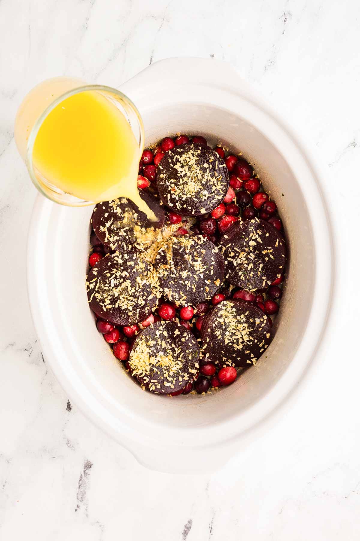 orange juice pouring from glass measuring jug over cranberry sauce in crock