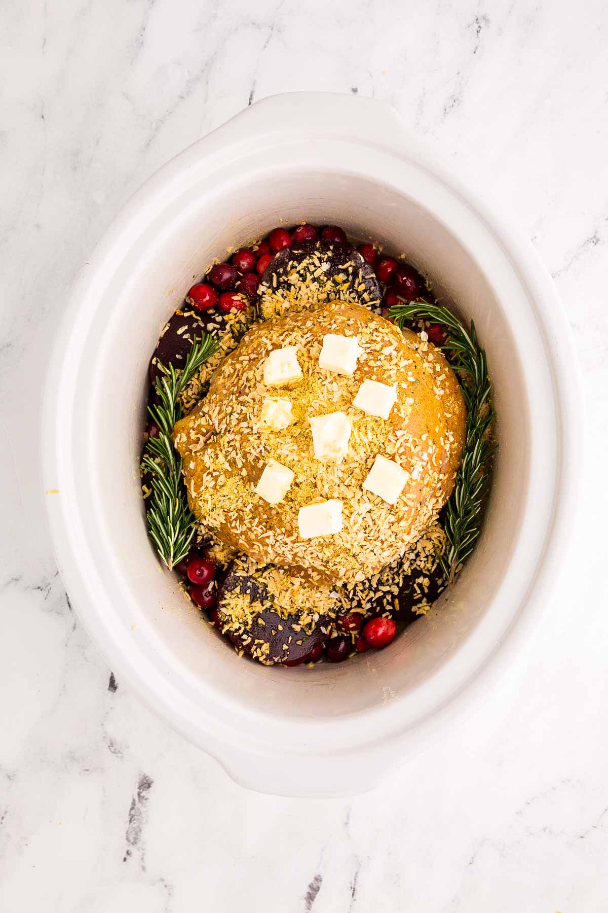 overhead view of turkey breast in crock with sliced butter and rosemary sprigs