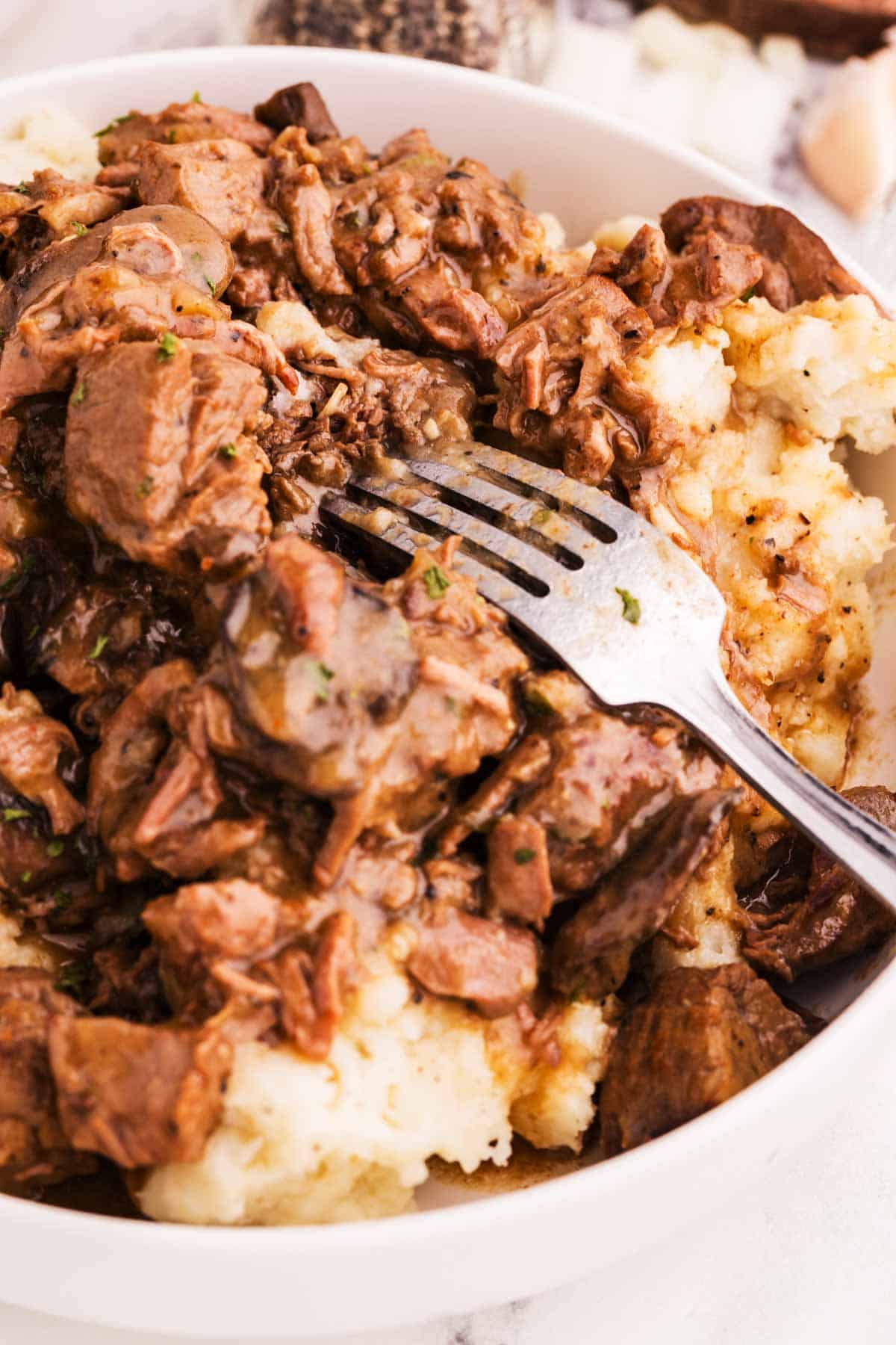 close up photo of fork in mound of mashed potatoes and beef tips with gravy