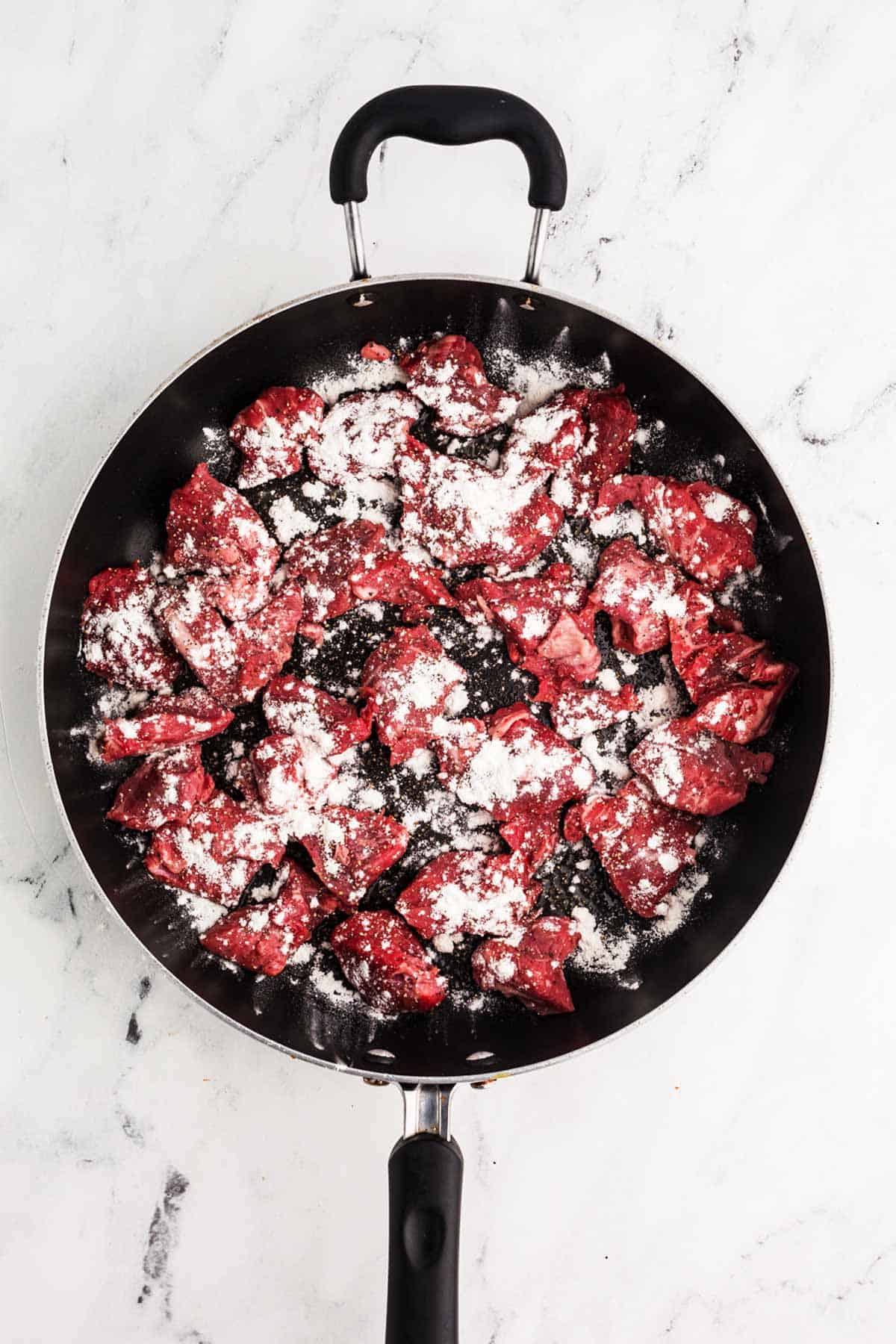 overhead view of raw beef and flour in skillet