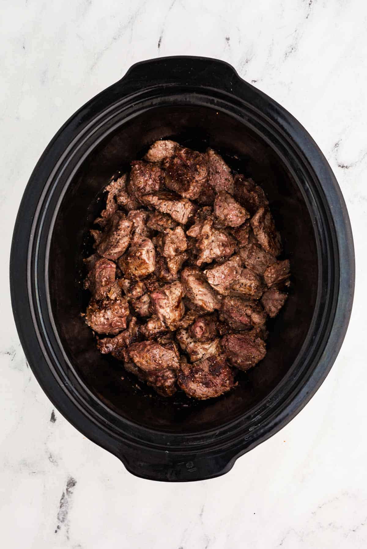 overhead view of seared beef in slow cooker