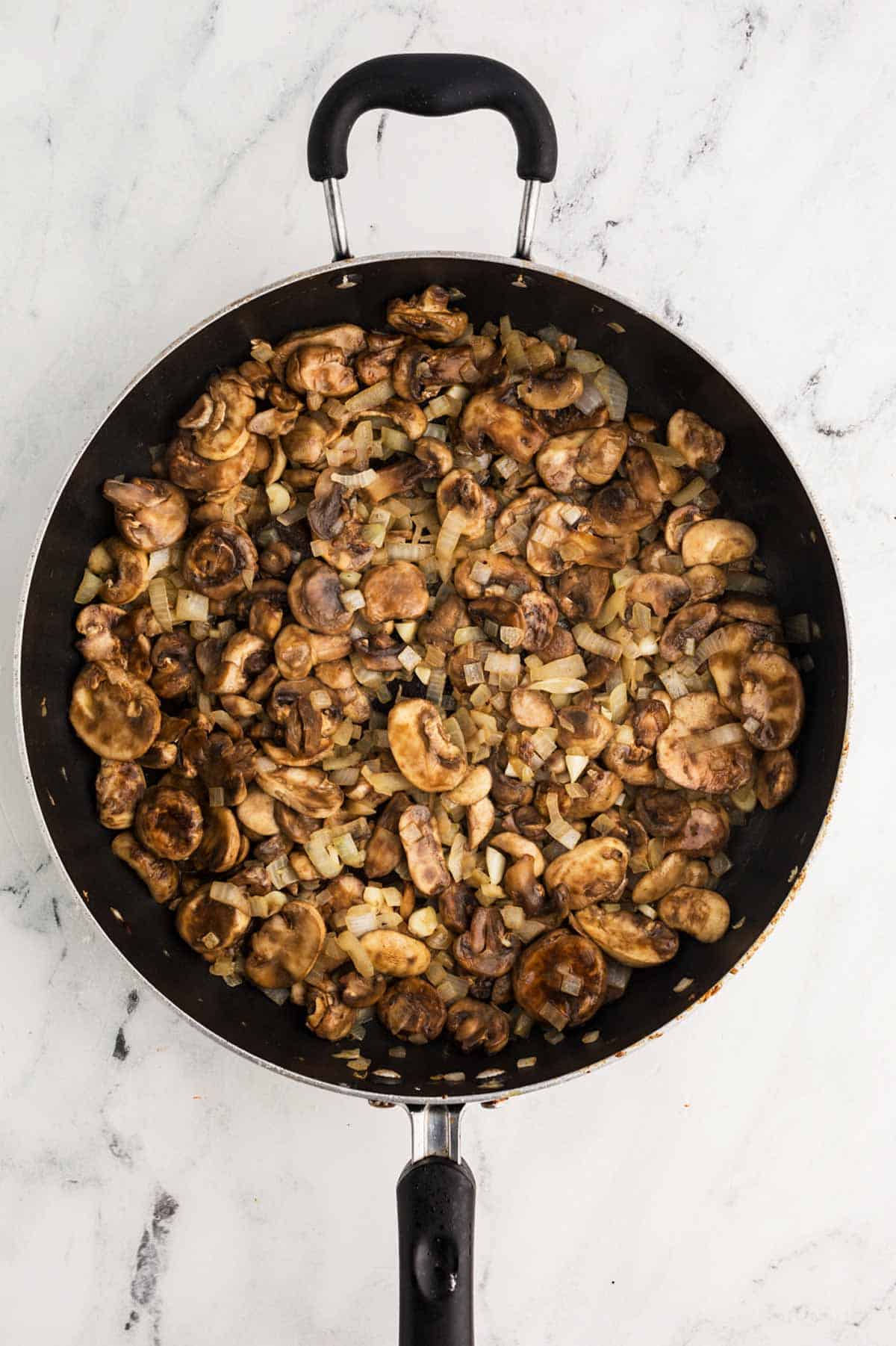 overhead view of uncooked mushrooms and onion in skillet