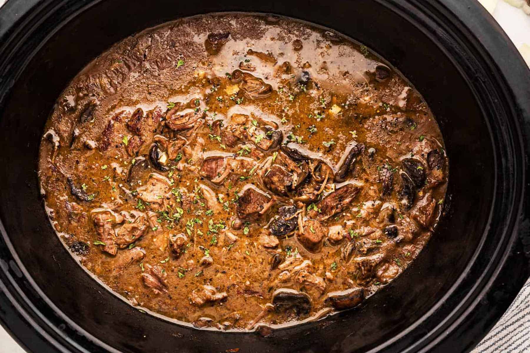 overhead close up view of beef tips and mushroom gravy in black crockery pot