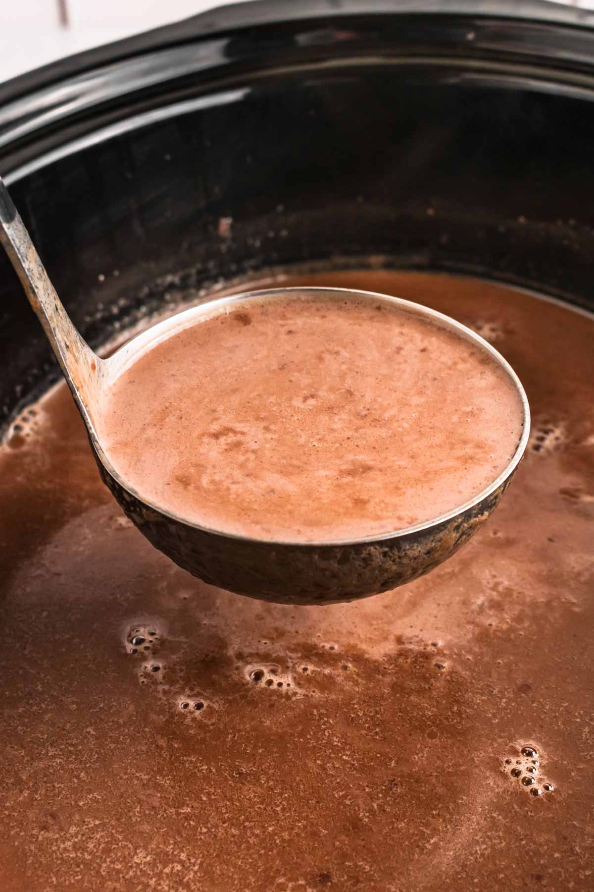 frontal view of ladle with hot chocolate in slow cooker