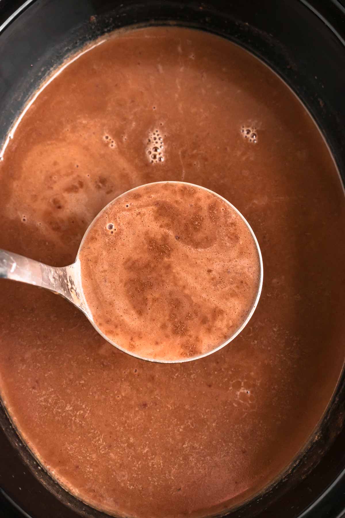 close up view of ladle over slow cooker with hot chocolate