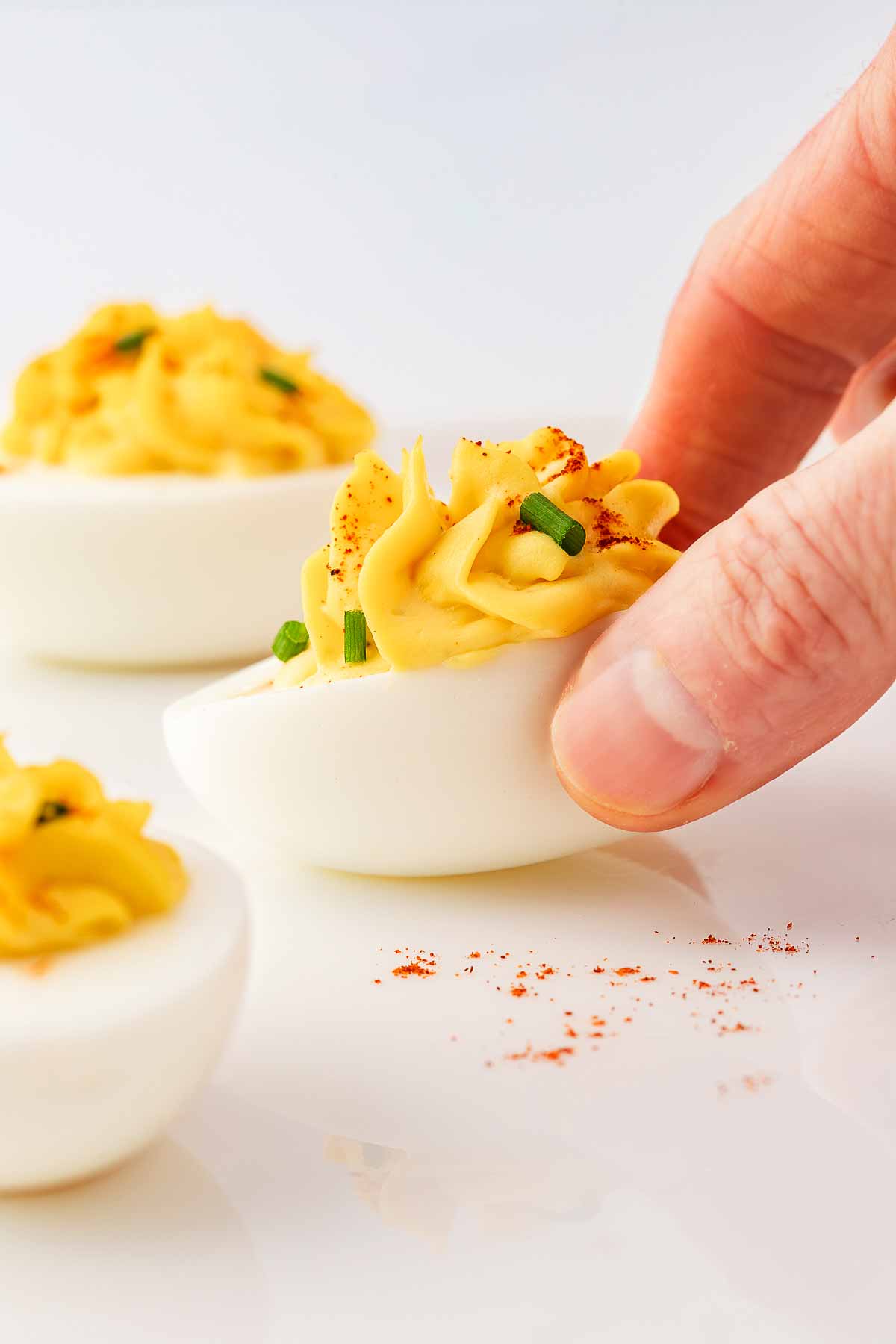 female hand picking up deviled egg from white plate