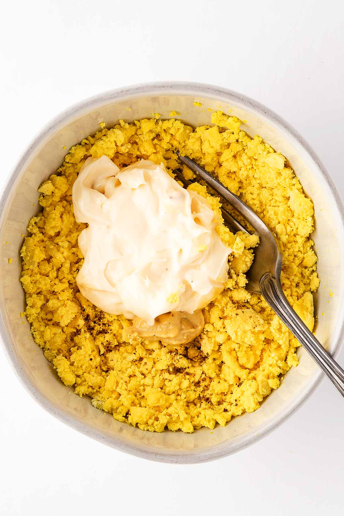 overhead view of white bowl with egg yolks and mayonnaise