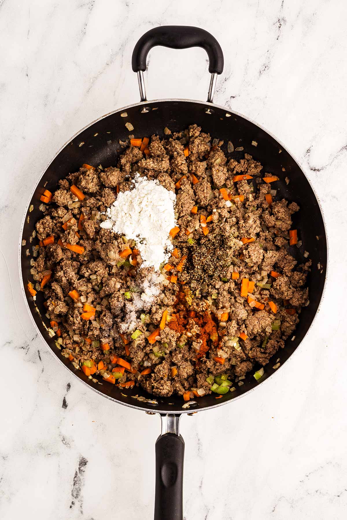 overhead view of browned ground beef mixture with salt, paprika, and flour in skillet