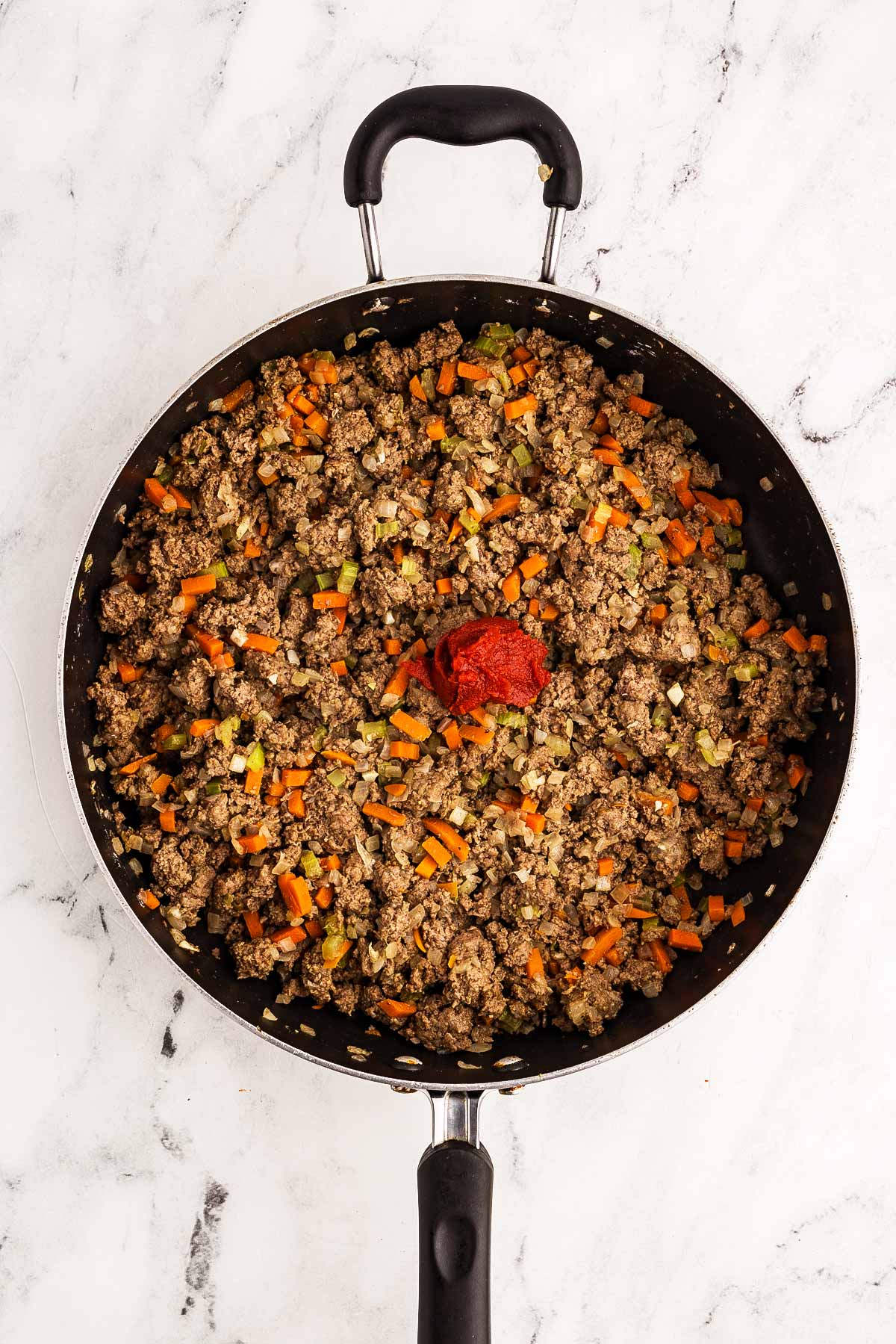 overhead view of shepherd's pie filling in skillet with spoonful of tomato paste on top