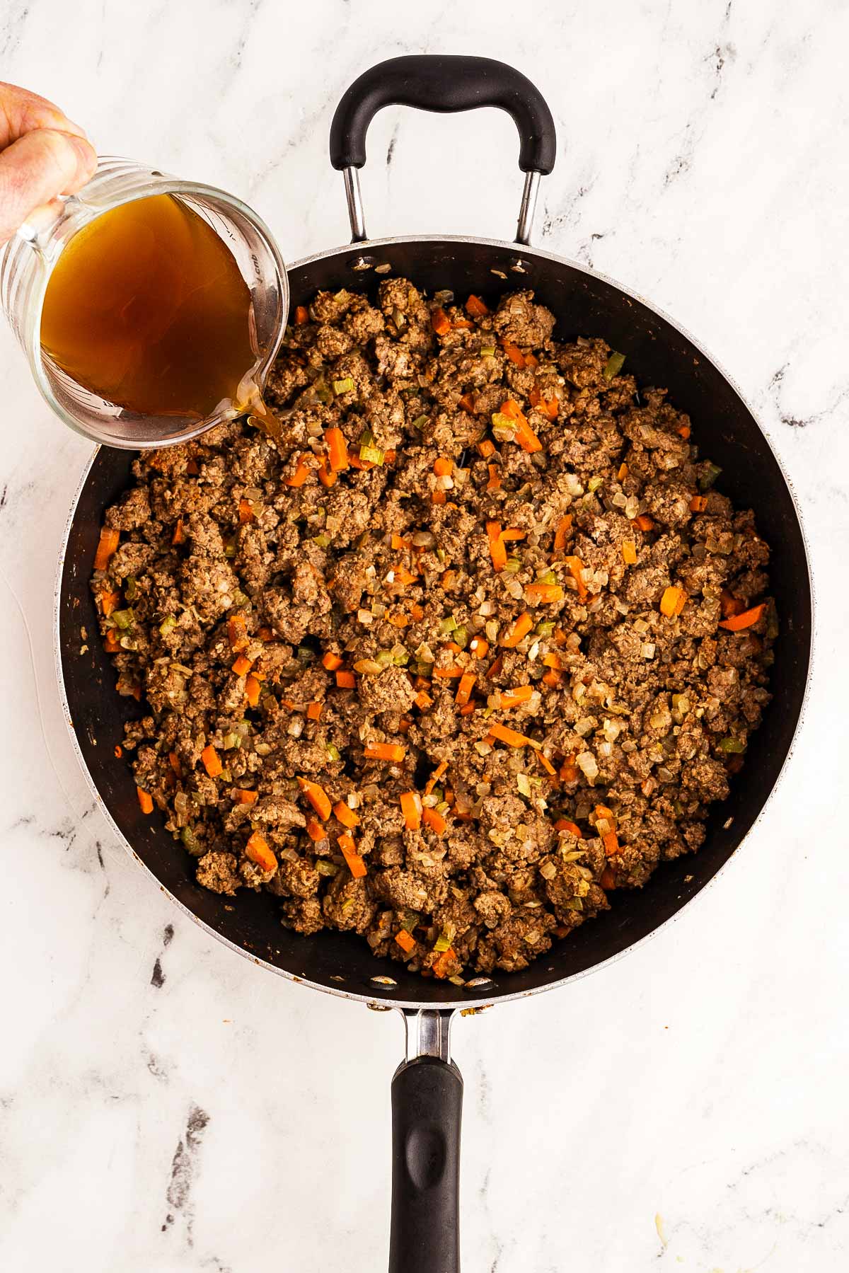 overhead view of beef broth pouring into skillet with ground beef mixture