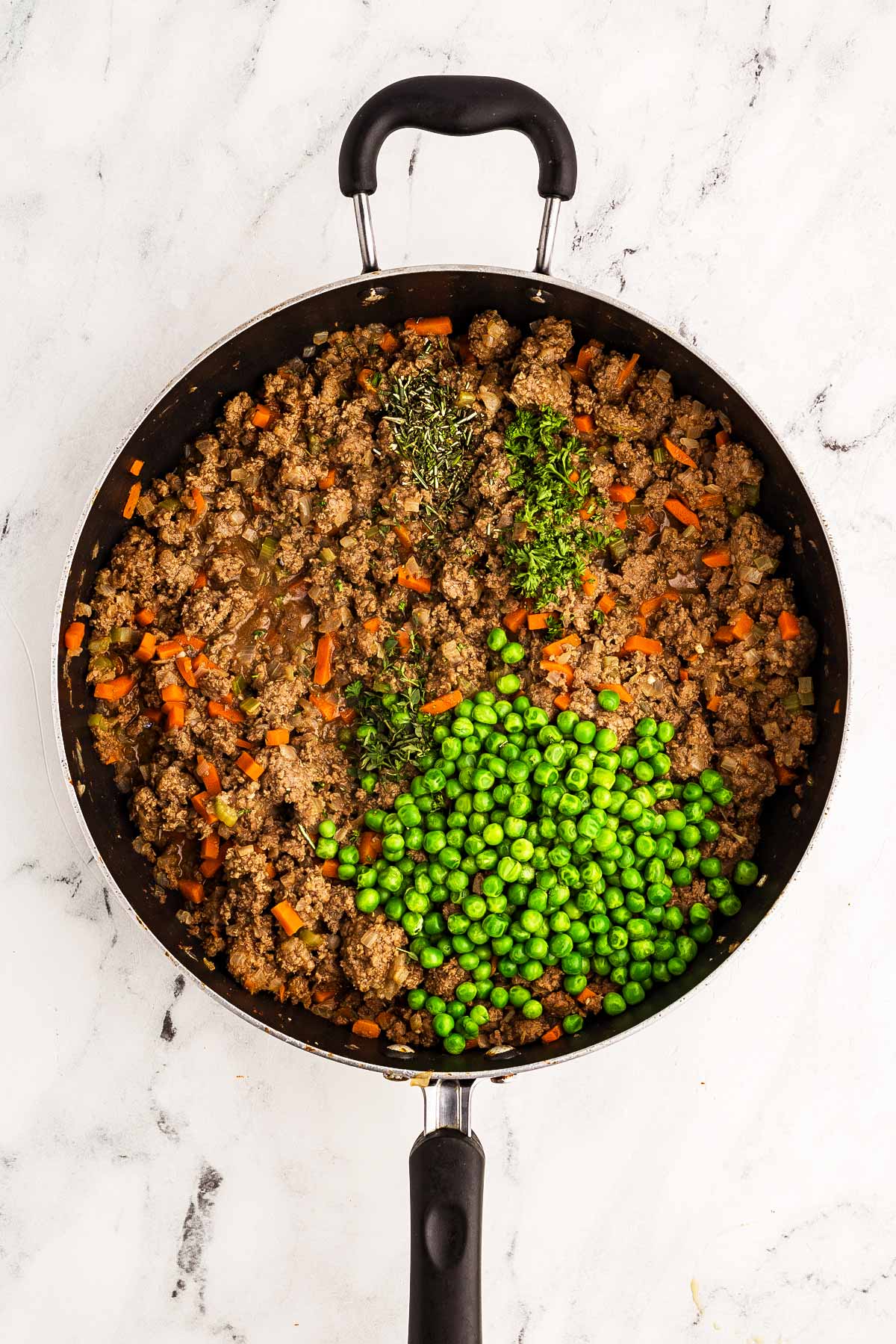 overhead view of simmering ground beef filling in skillet with broth, peas, and herbs