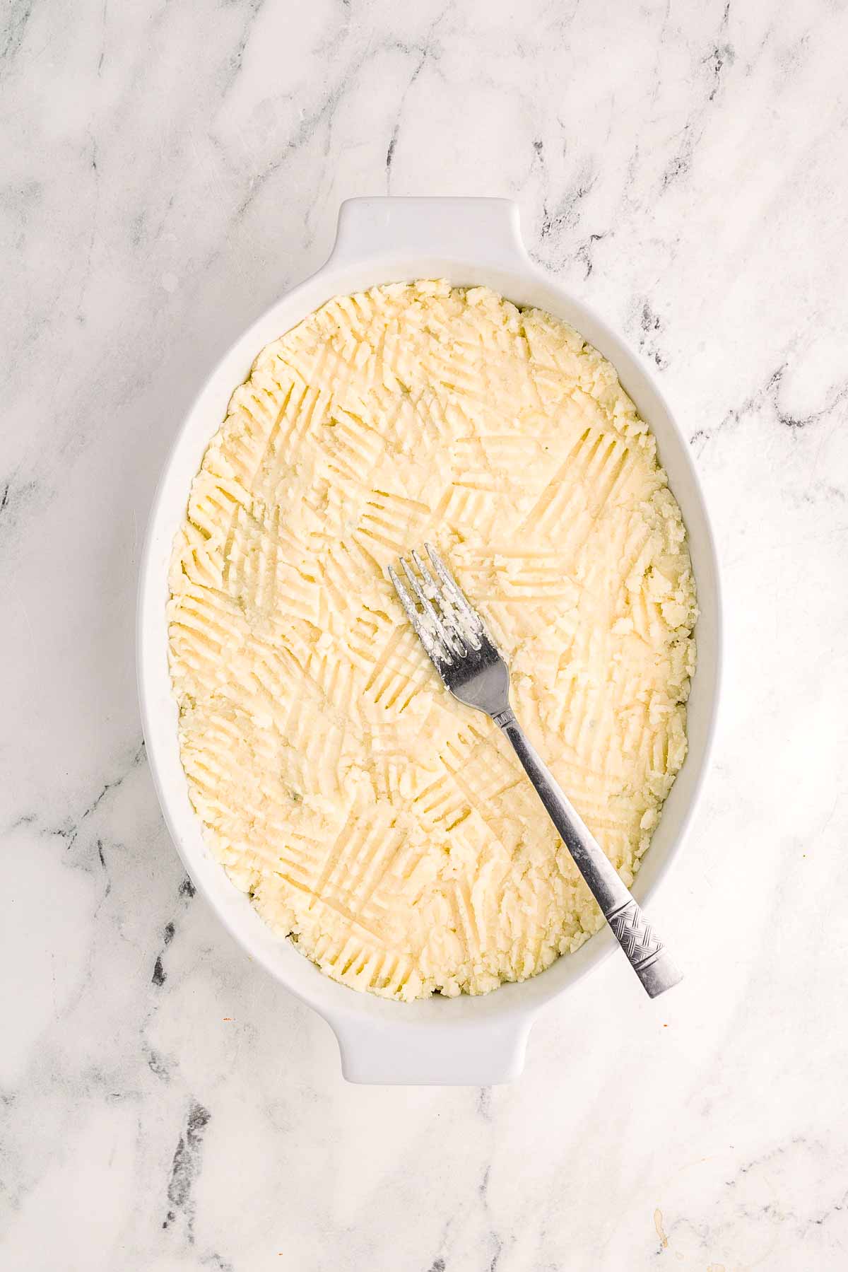 overhead view of mashed potatoes spread in white casserole dish with fork on top