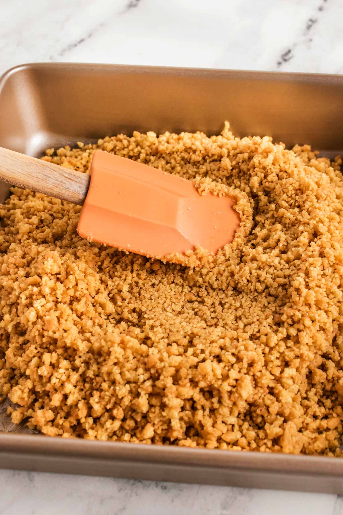 frontal view of spatula spreading cookie crumbs in square pan