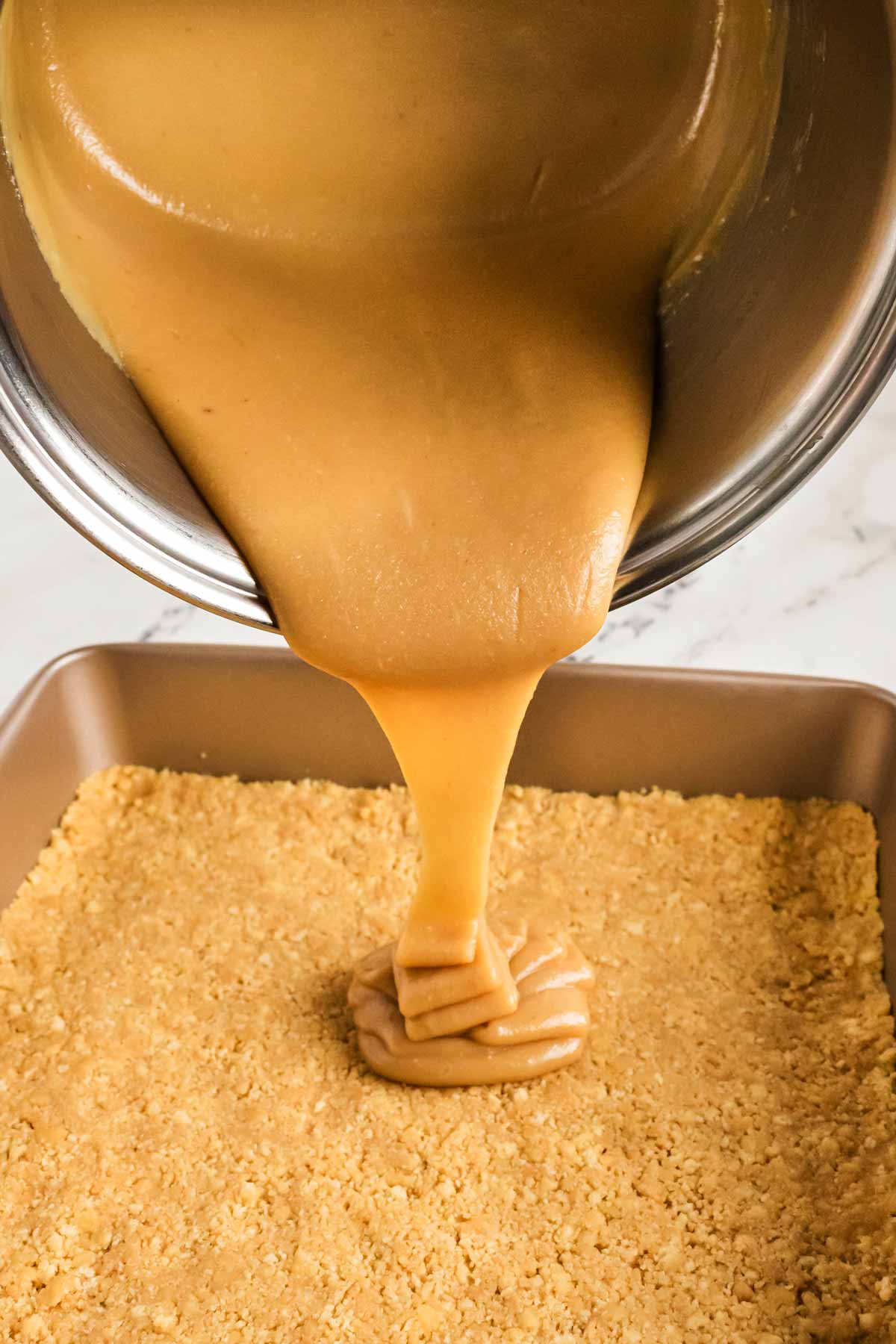 caramel pouring from saucepan over shortbread base in baking pan