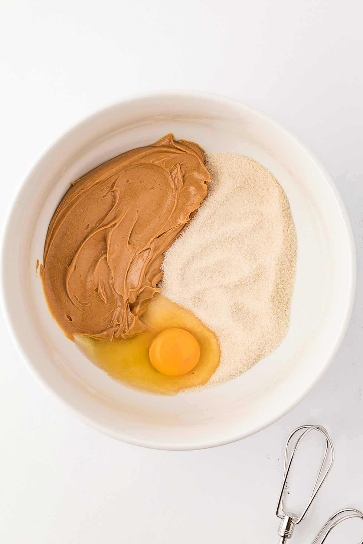 overhead view of peanut butter, sugar and egg in white bowl