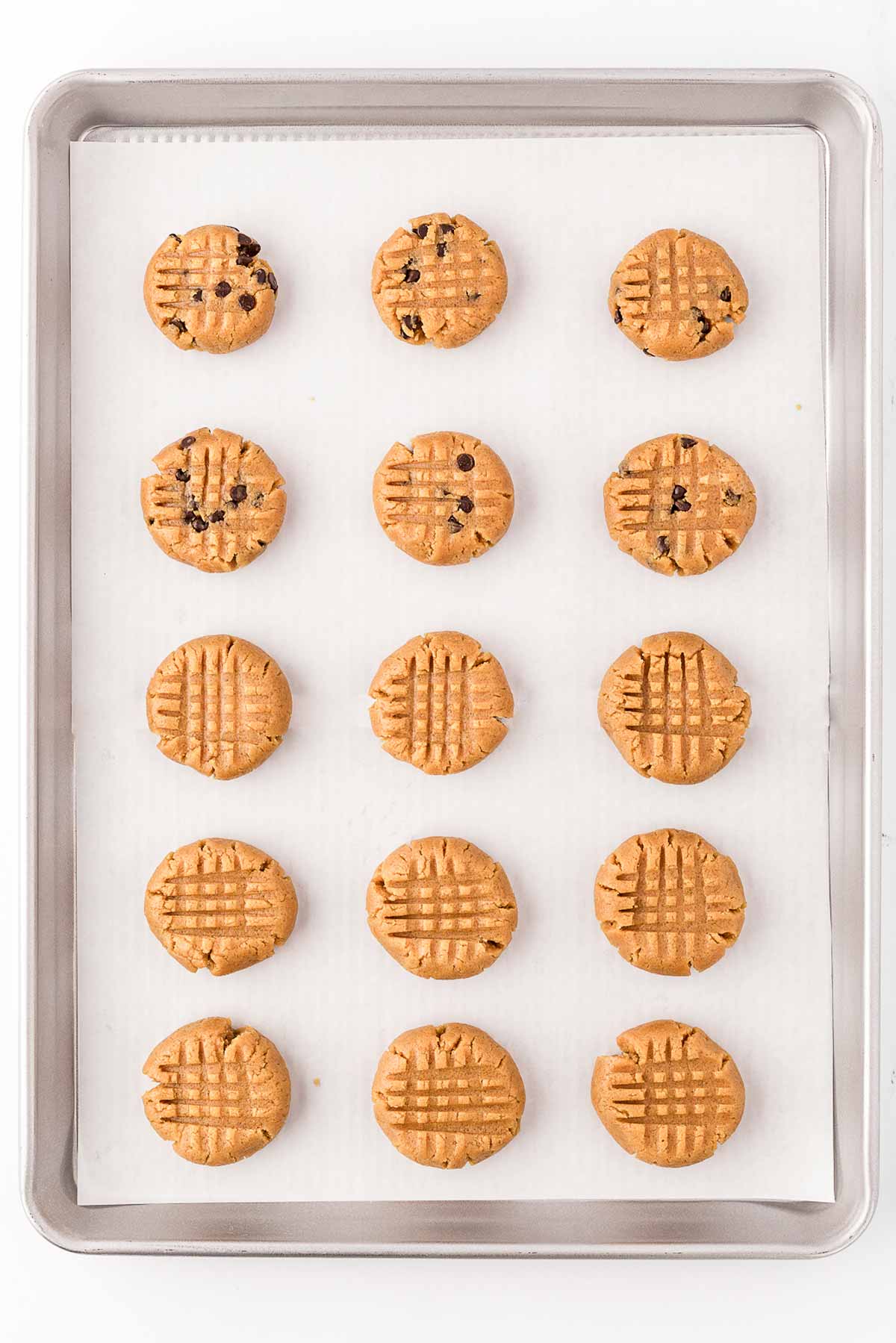 overhead view of unbaked peanut butter cookies on lined baking sheet