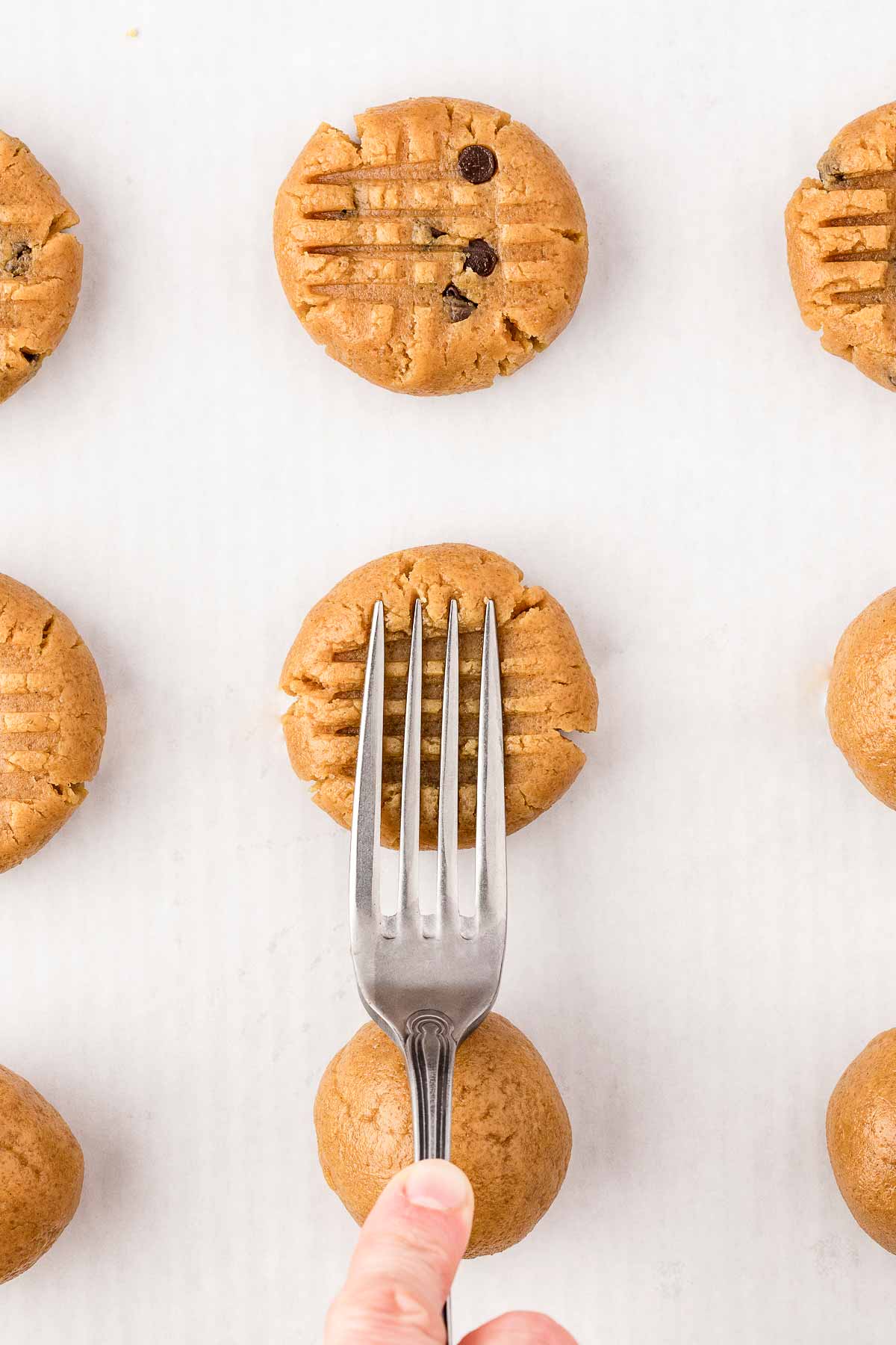 fork pressing down on peanut butter cookie to create criss cross pattern