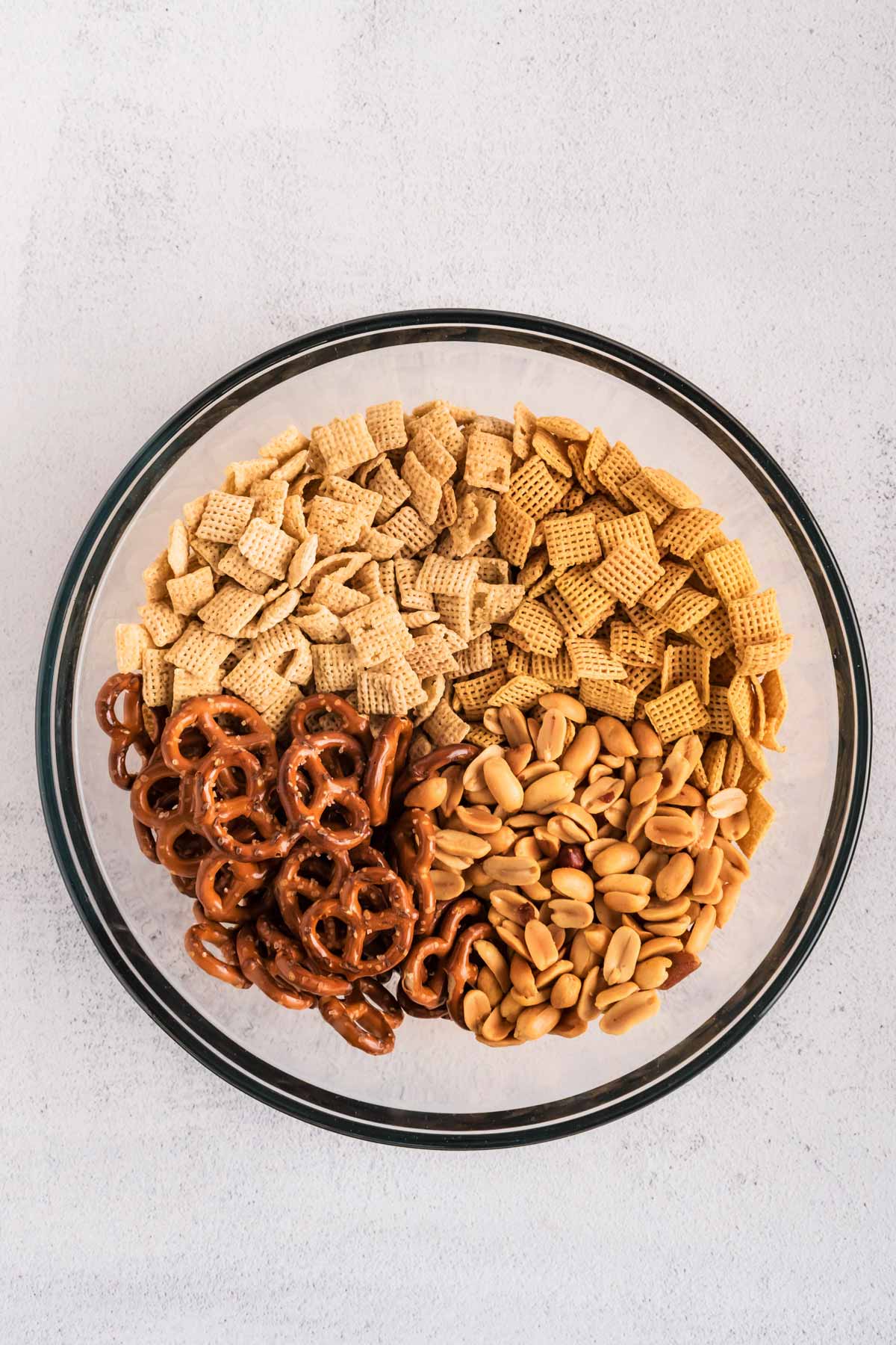 overhead view of Chex cereal, pretzels and peanuts in glass bowl