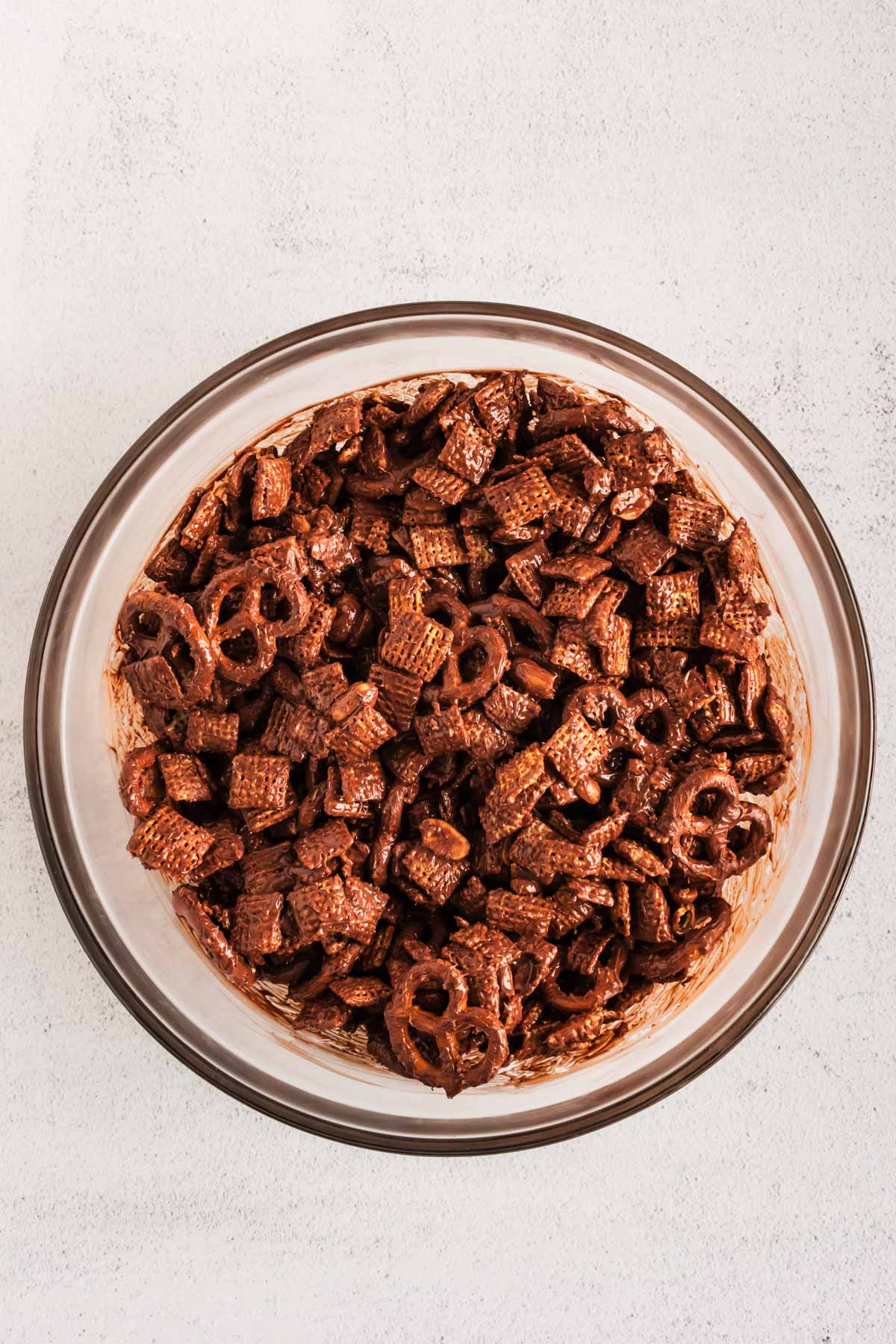 overhead view of chocolate covered pretzels, peanuts and cereal in glass bowl