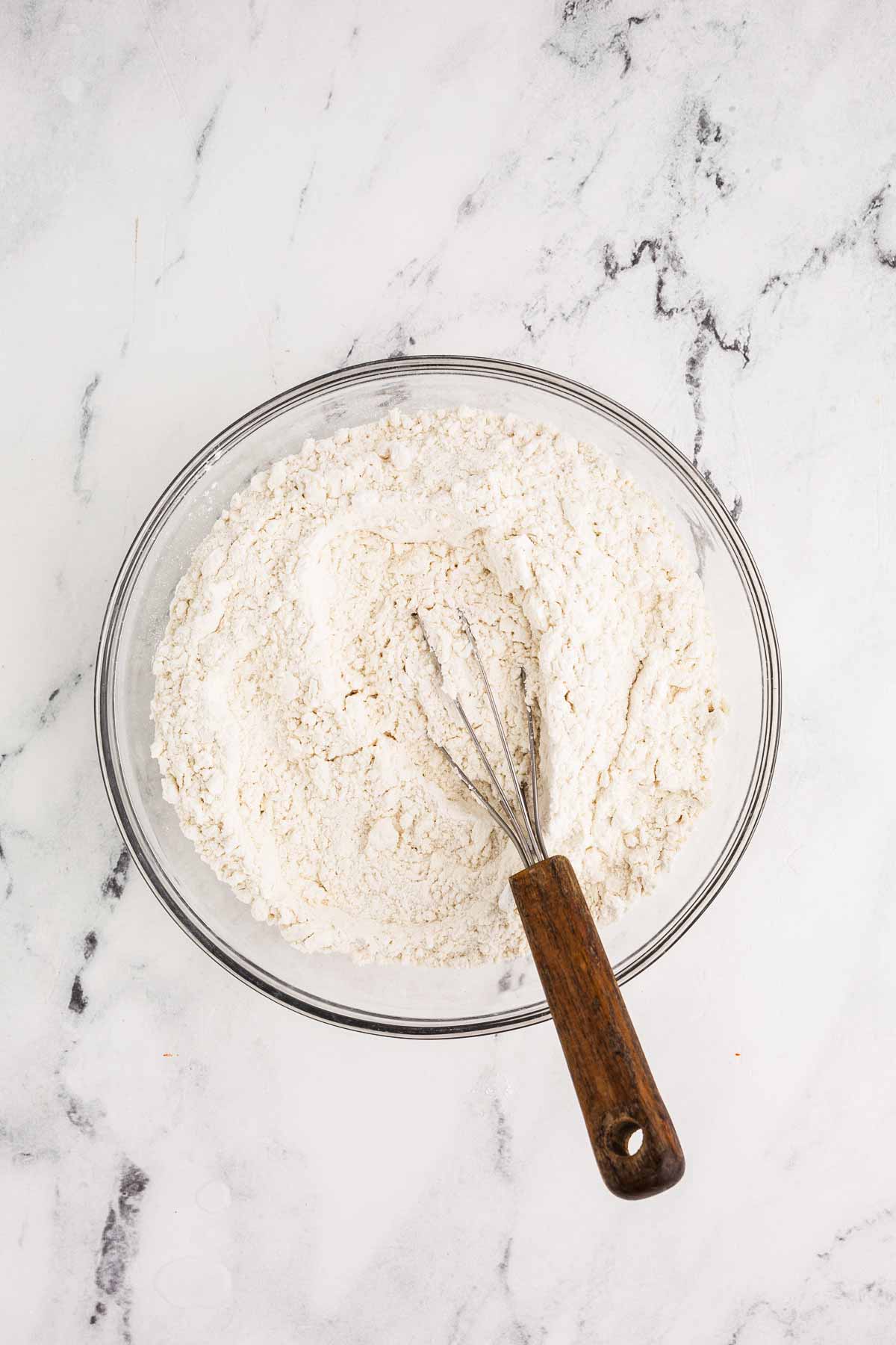 overhead view of flour in glass bowl with whisk