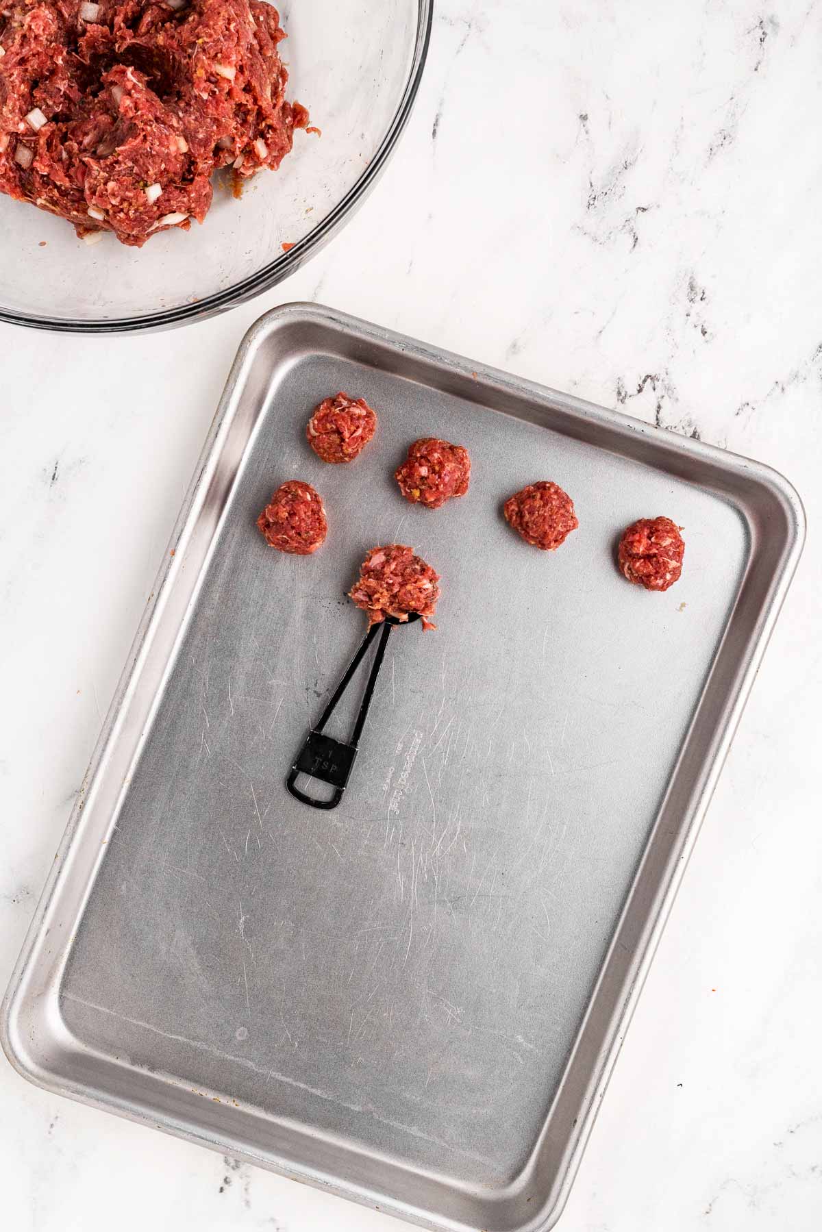 overhead view of uncooked meatballs on sheet pan